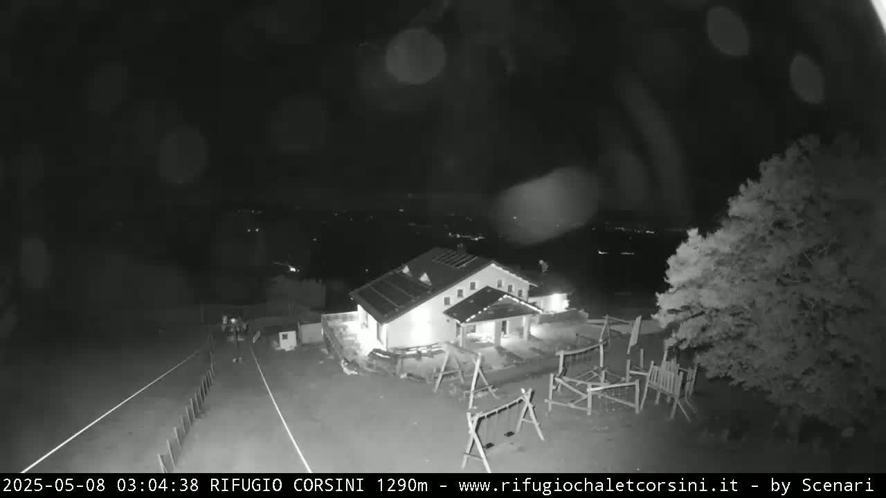 A nighttime, possibly rainy, black and white view of a building with a playground and surrounding trees.
