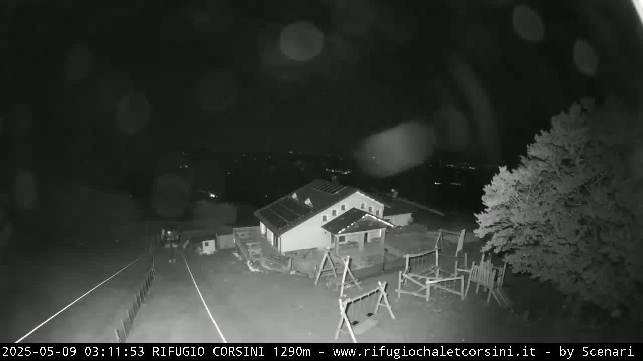 A nighttime, low-light image shows a building with a playground and trees, under possibly rainy conditions.