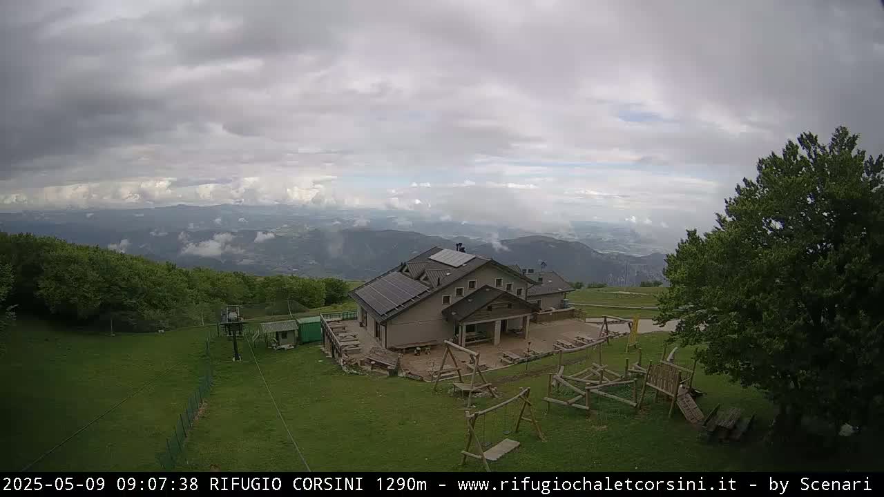 A mountaintop lodge with a playground sits below an overcast sky, overlooking a valley shrouded in mist.