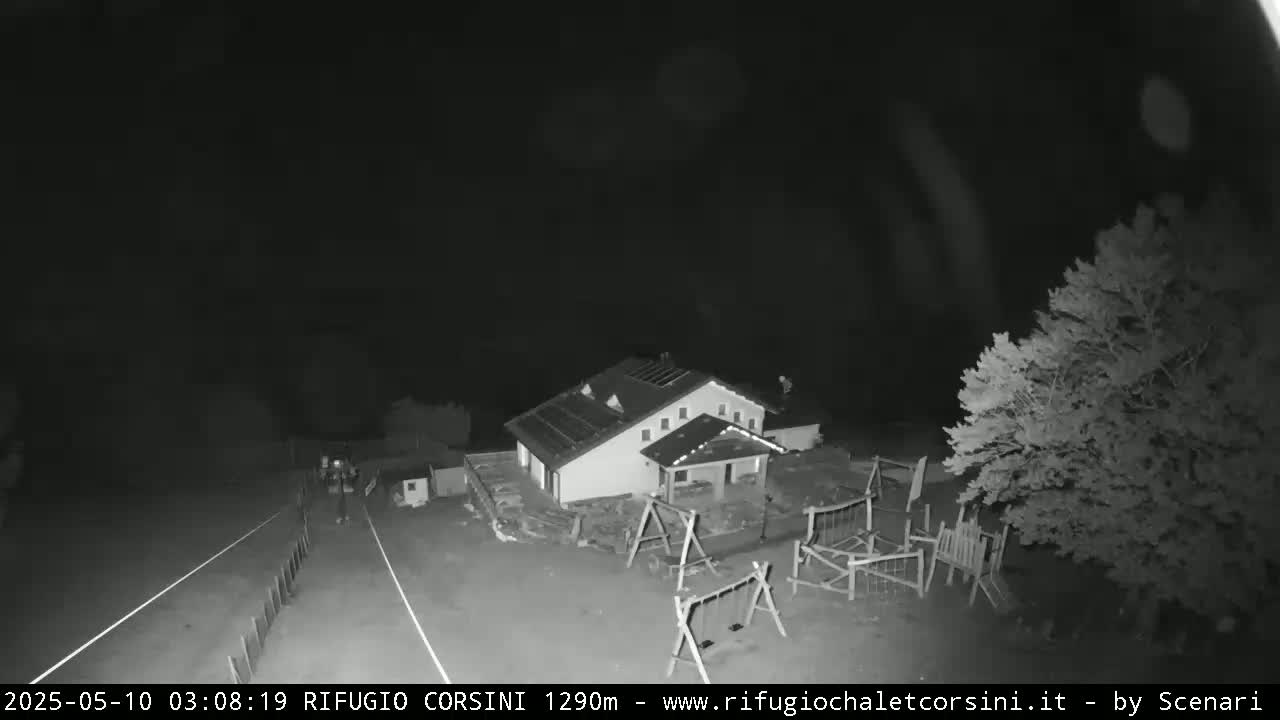 A nighttime, black-and-white overhead view shows a building with a playground next to a road.