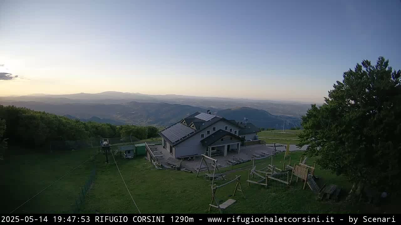 A mountaintop building with solar panels on the roof and a playground sits overlooking a vast valley at sunset under a clear sky.