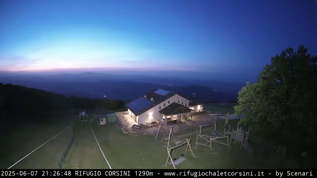 A mountaintop building with a playground is illuminated at dusk under a clear, dark blue sky, overlooking a hazy valley.