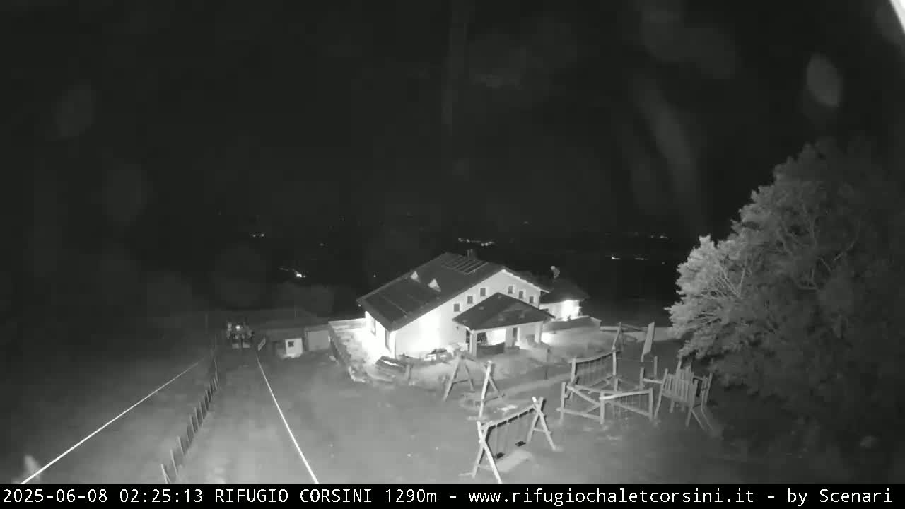 A nighttime, infrared view shows a building with lights on, a playground, and a road leading away from the scene.