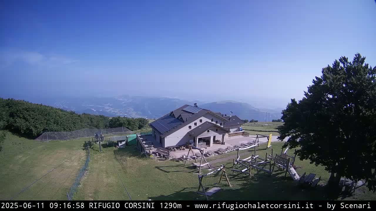 A mountaintop building with solar panels sits beside a playground, overlooking hazy mountains under a clear blue sky.