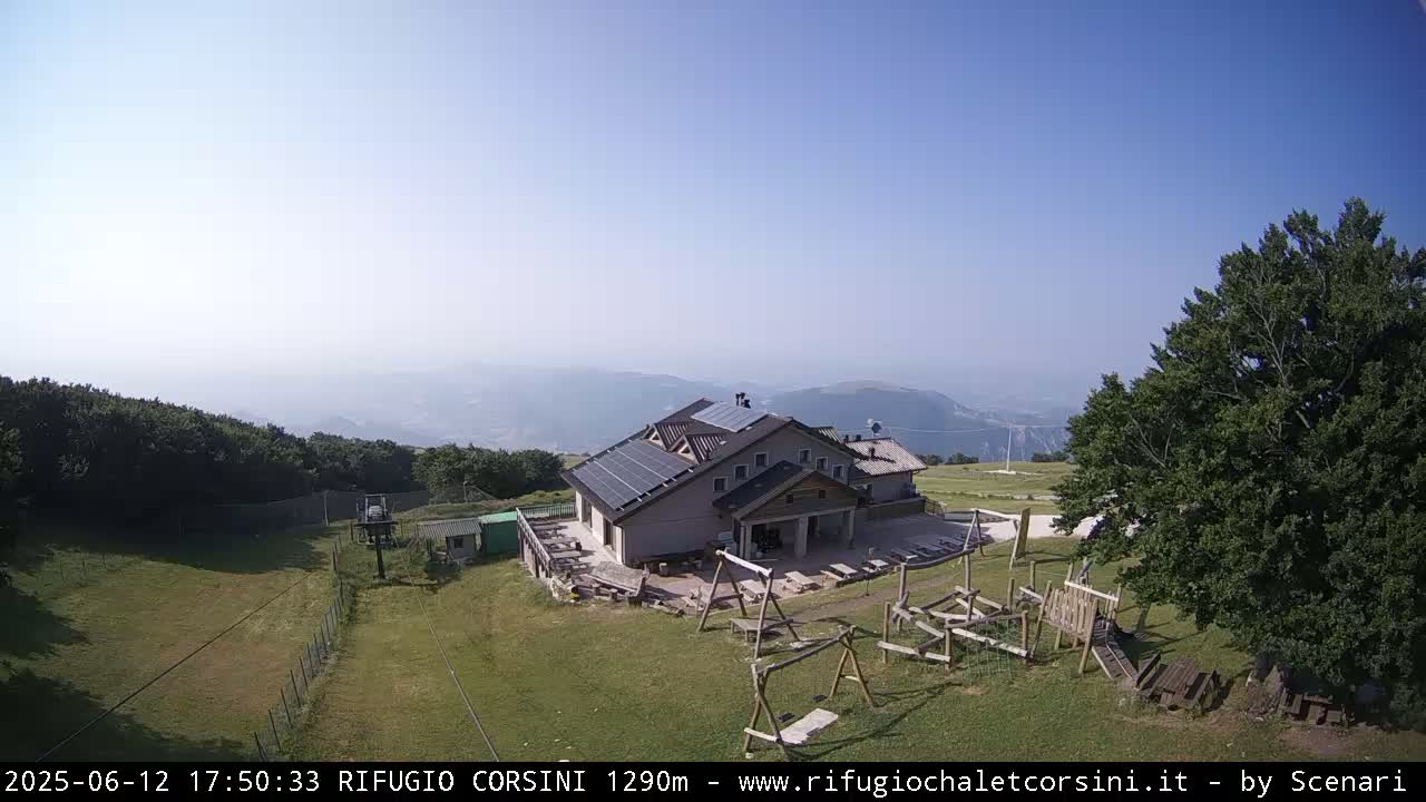 A mountaintop building with solar panels, a playground, and a chairlift is visible on a hazy, sunny day.