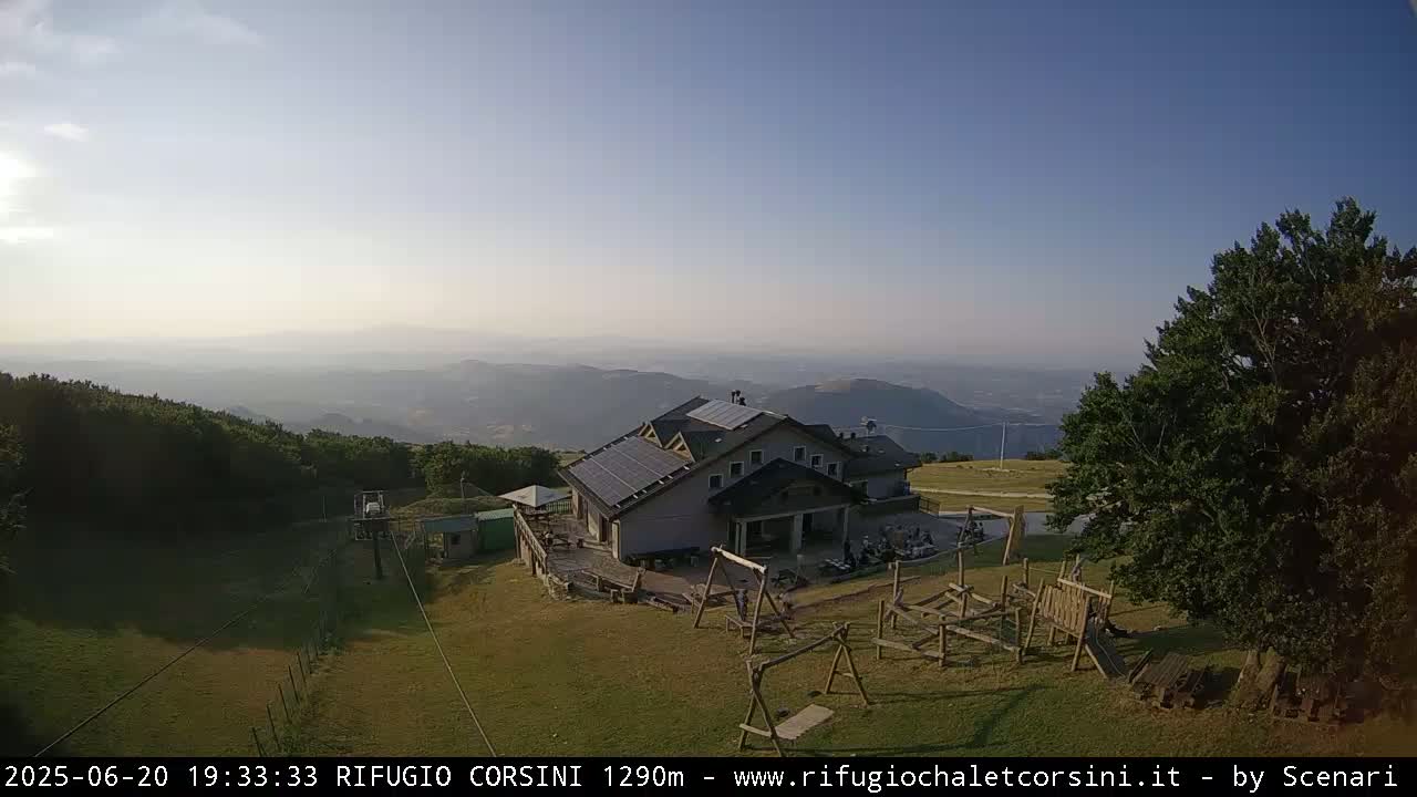 A mountaintop building with solar panels sits beside a playground, overlooking a hazy valley under a clear sky.