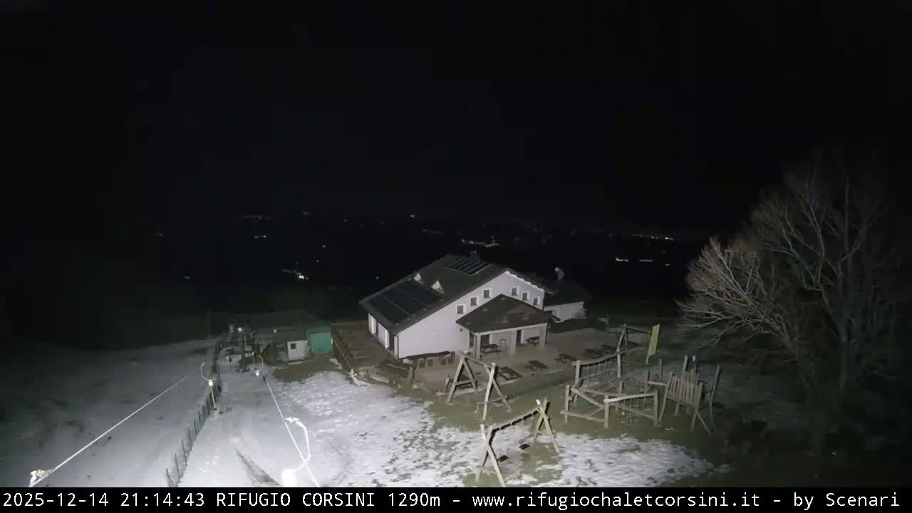 A snow-covered ski resort area, featuring a large lodge with solar panels, a ski lift, and wooden playground equipment, is enveloped in thick fog under overcast skies.