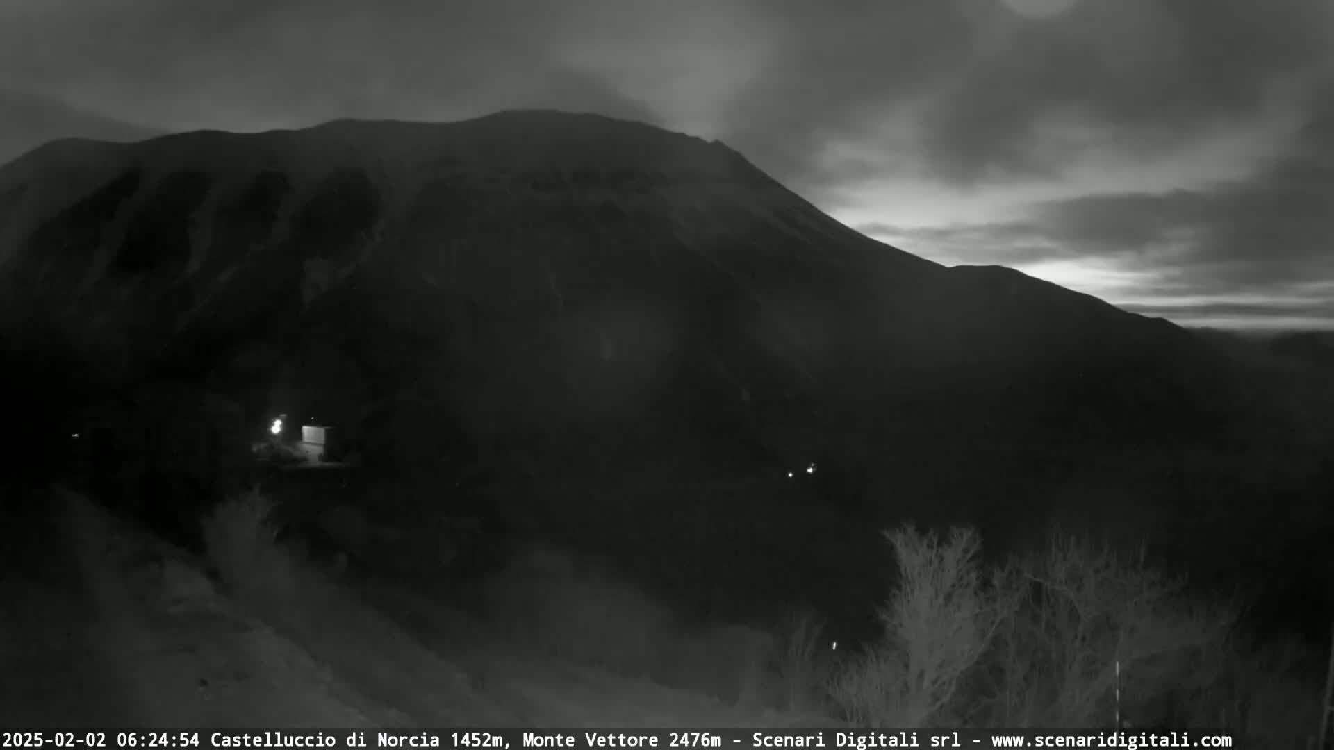A dark, mountainous landscape is visible at twilight under a cloudy sky.