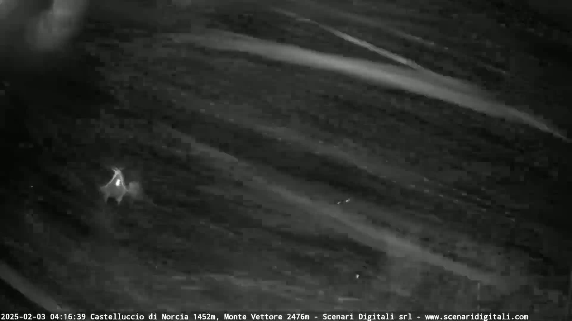 A nighttime, low-light image shows a small, bright object amidst streaks of light against a dark background, possibly indicating clouds or atmospheric phenomena.
