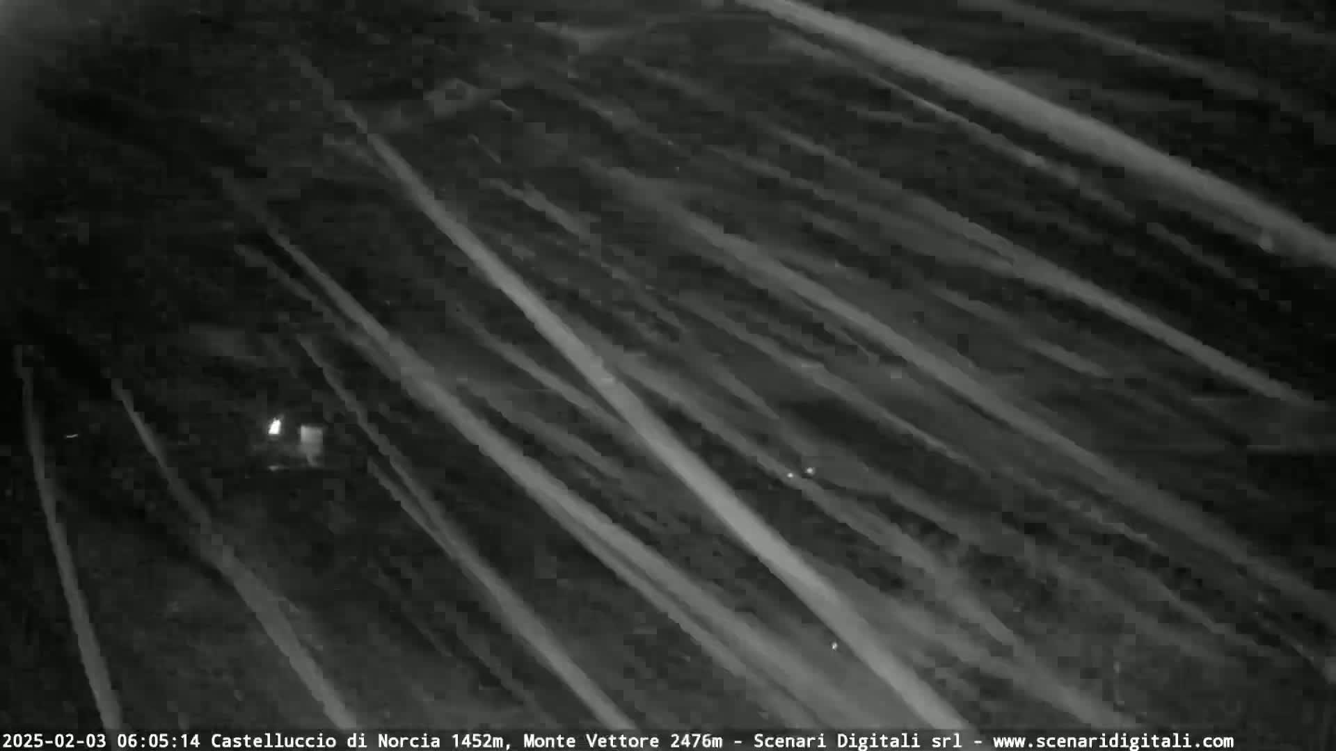 A nighttime, low-light image shows diagonal streaks of light against a dark background, possibly indicating heavy snowfall or a similar weather event.