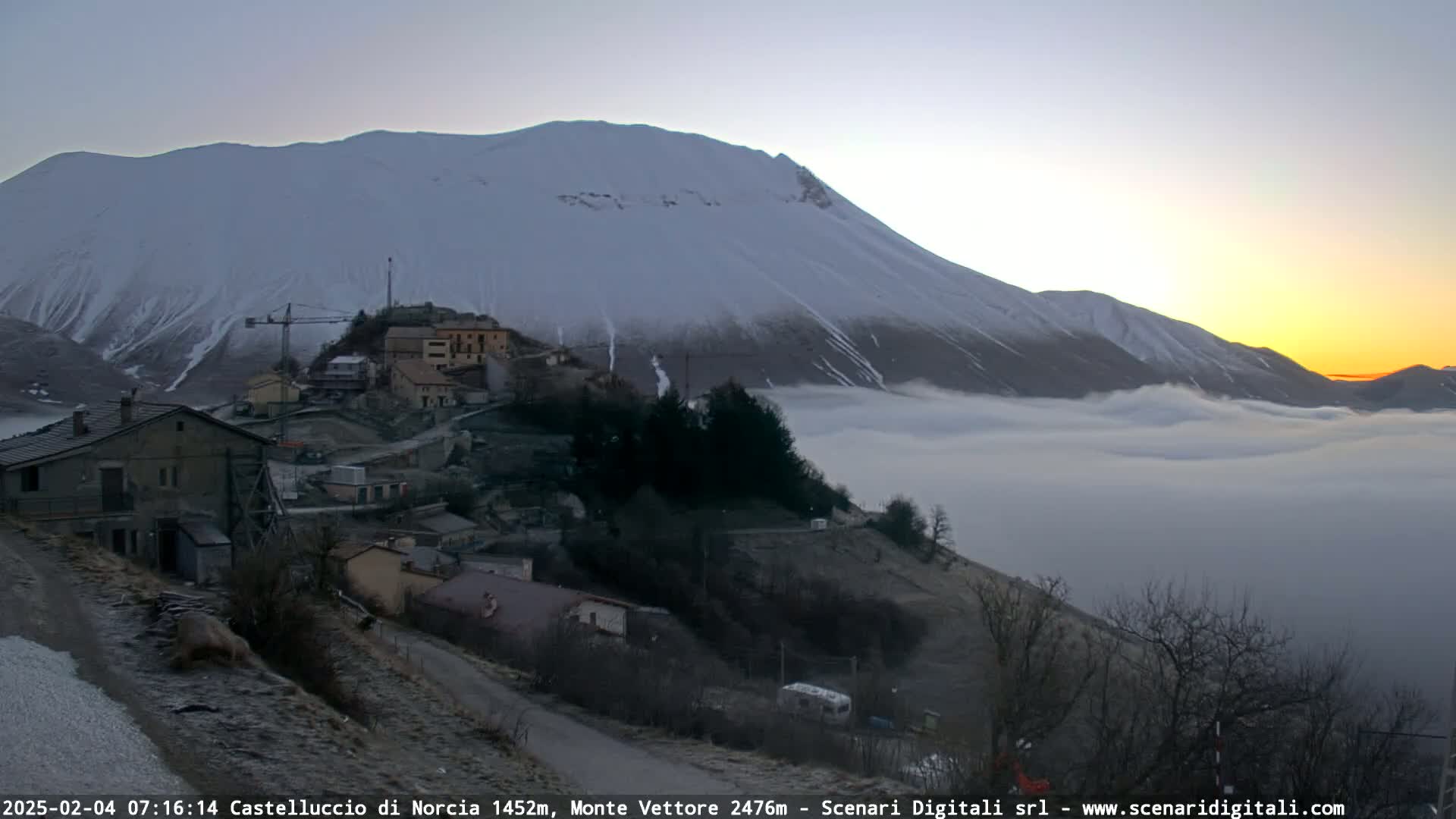 A snow-covered mountain is seen at sunrise over a small town nestled in a valley filled with fog.