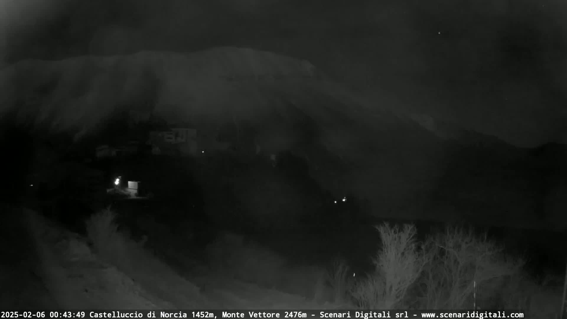 A snow-covered mountain looms in the dark under a clear night sky, overlooking a small village with a few scattered lights.