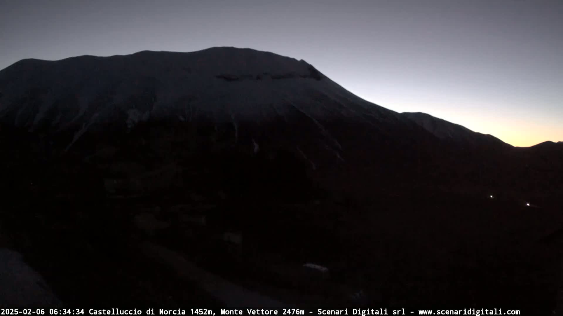 A snow-capped mountain is silhouetted against a dusky twilight sky.