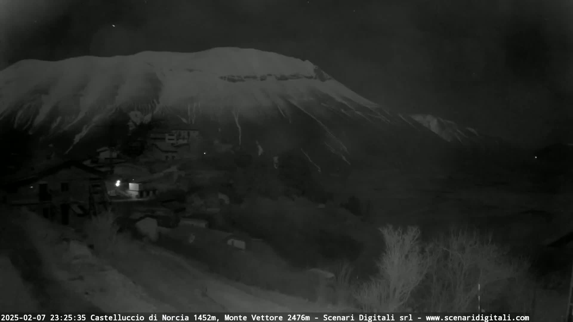 A snow-covered mountain looms over a small village at night.