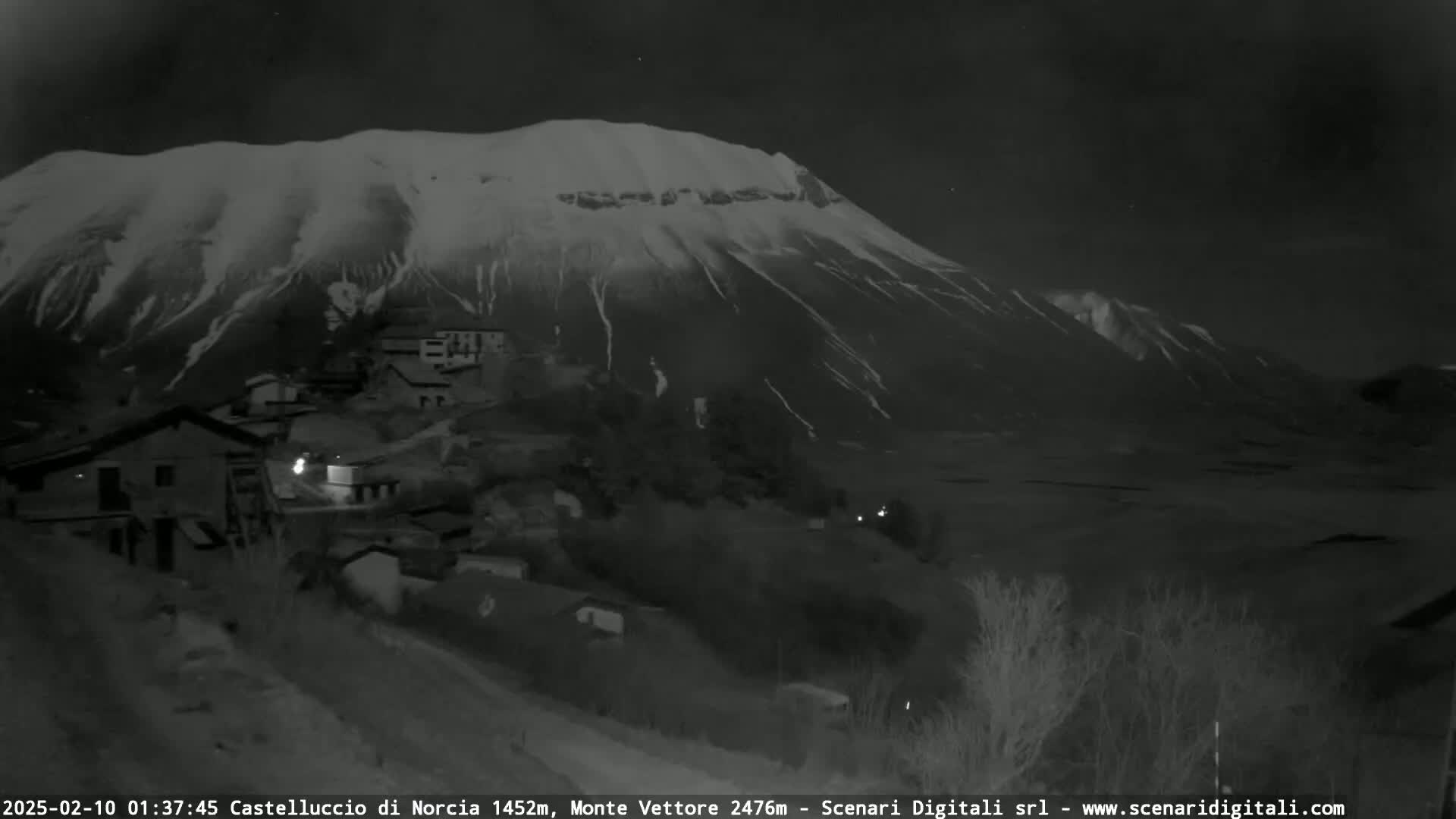 A snow-covered mountain looms over a small village at night.