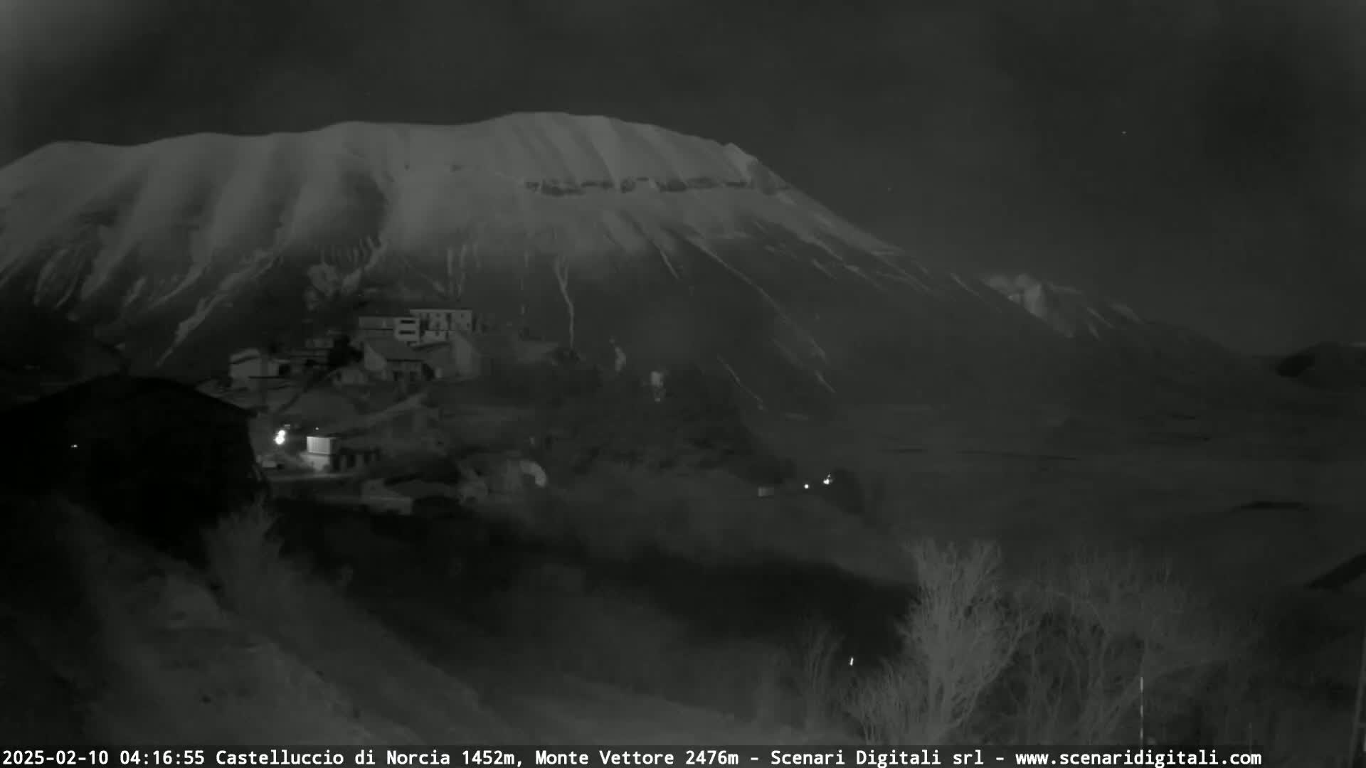 A snow-covered mountain looms over a small village at night.