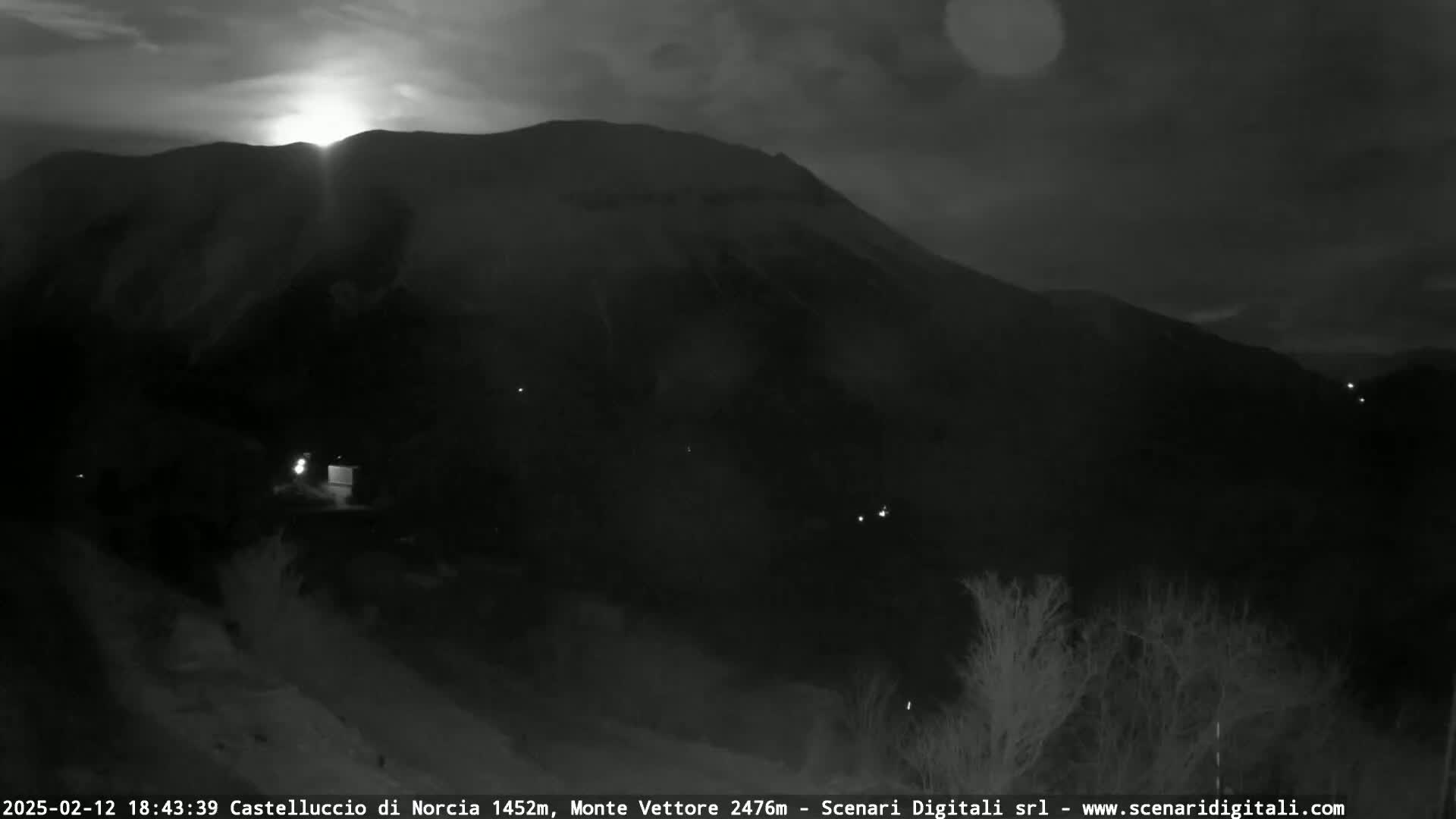 A nighttime, low-light view of a large, dark mountain silhouetted against a faintly bright sky.