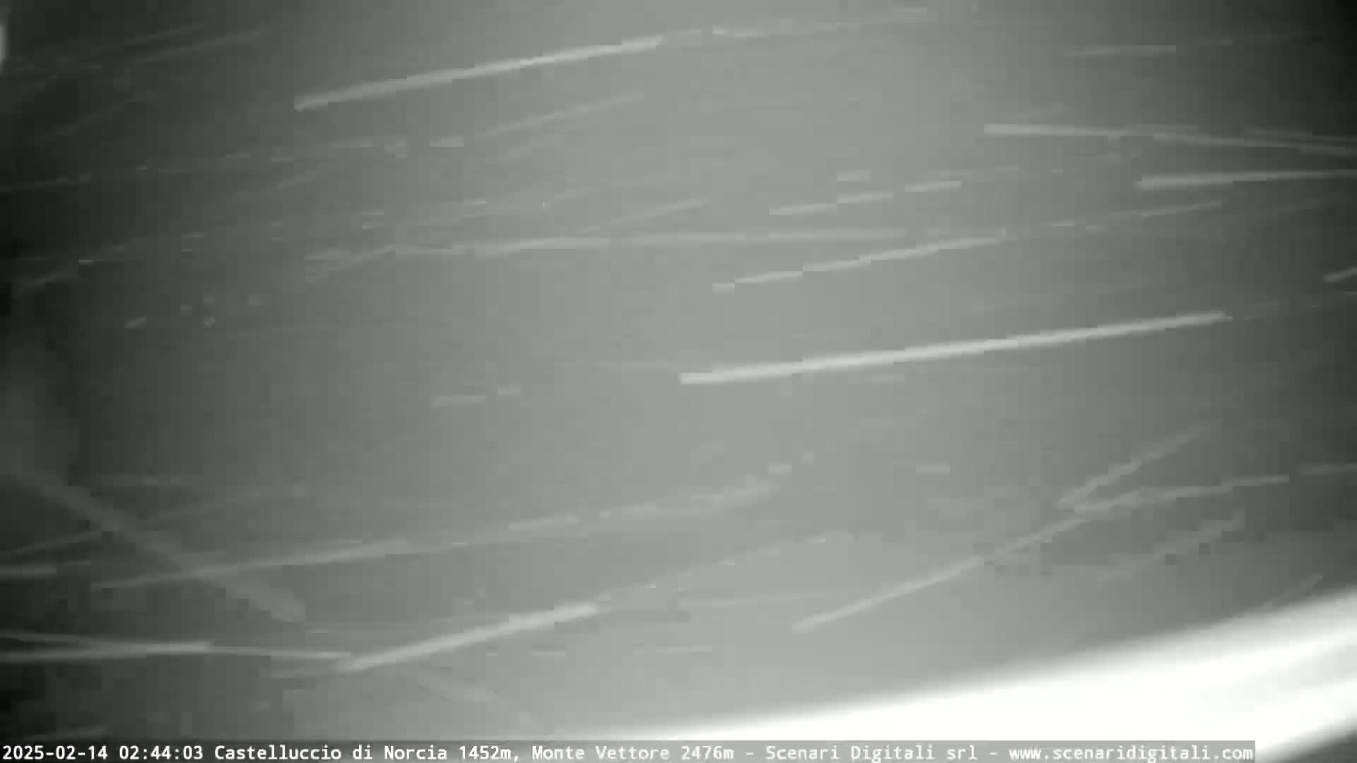 A nighttime, outdoor scene of light streaks across a dark gray background, indicating snow or other precipitation falling in the wind.