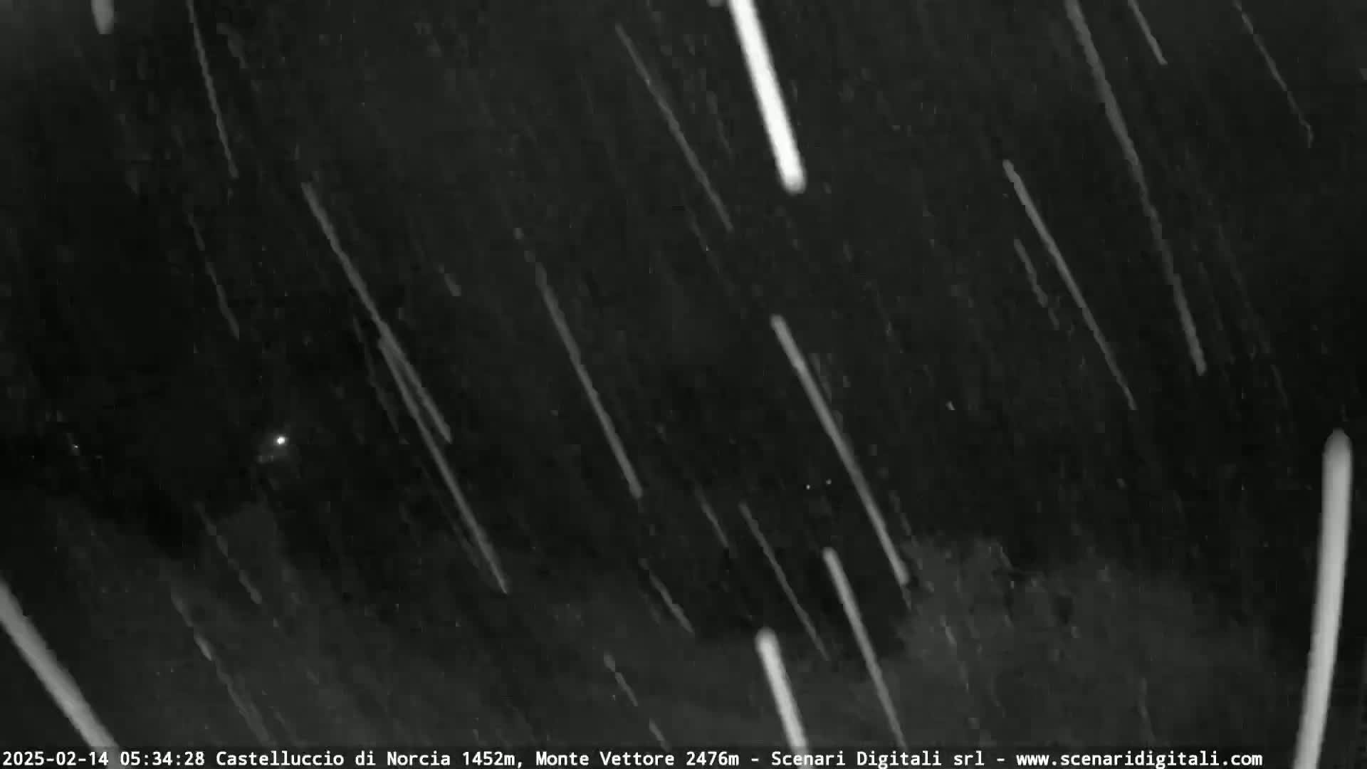 A nighttime, outdoor scene shows numerous streaks of light falling across a dark sky, possibly snow or meteors.
