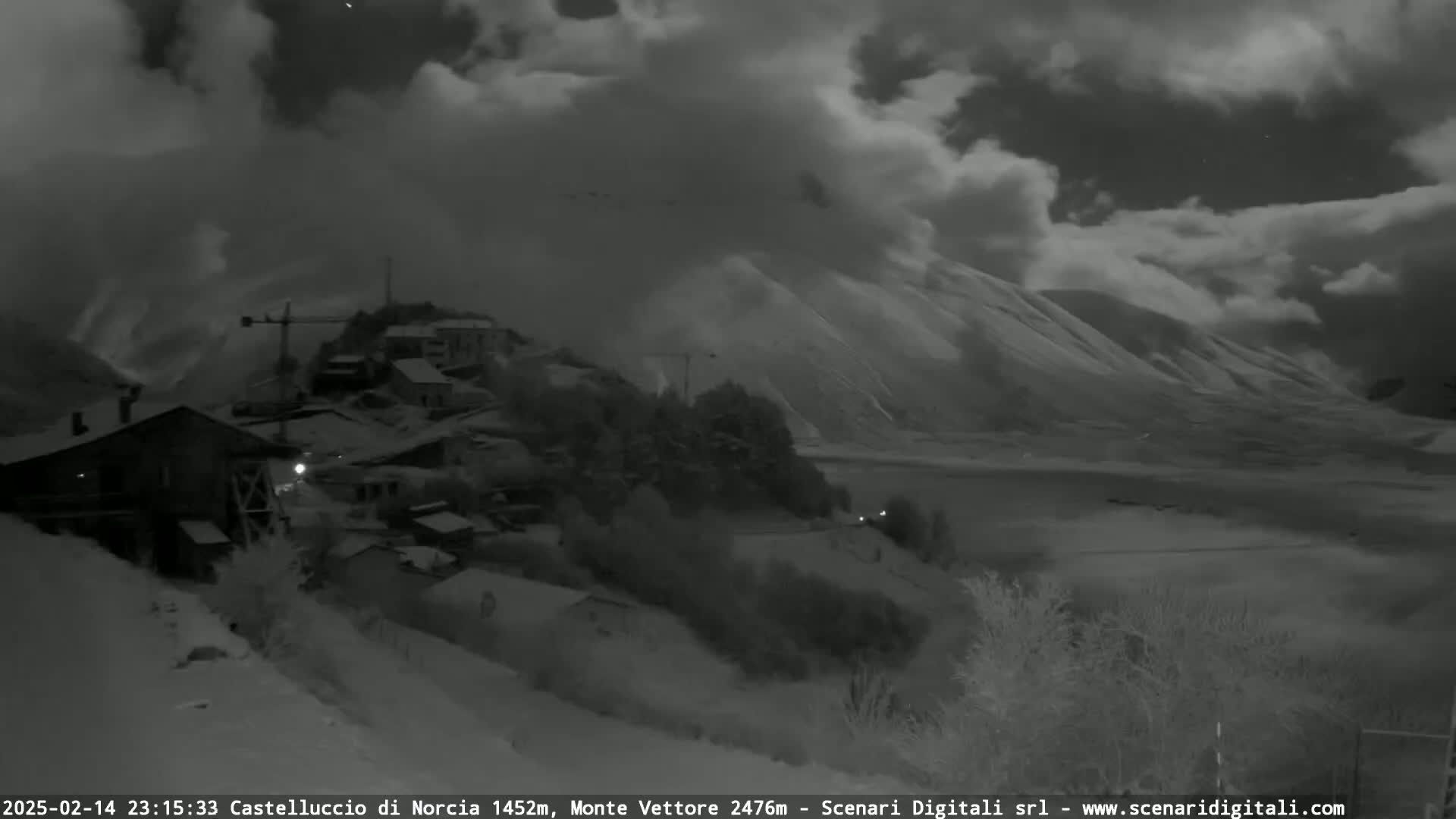 A snow-covered village nestled in a valley under a cloudy night sky.