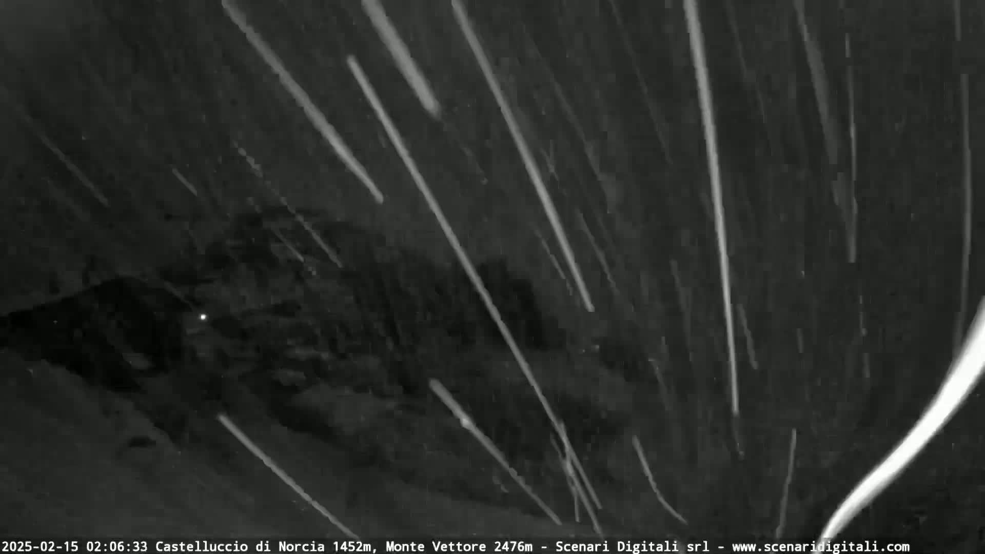 A nighttime, outdoor scene shows heavy snowfall over a dark, mountainous landscape.