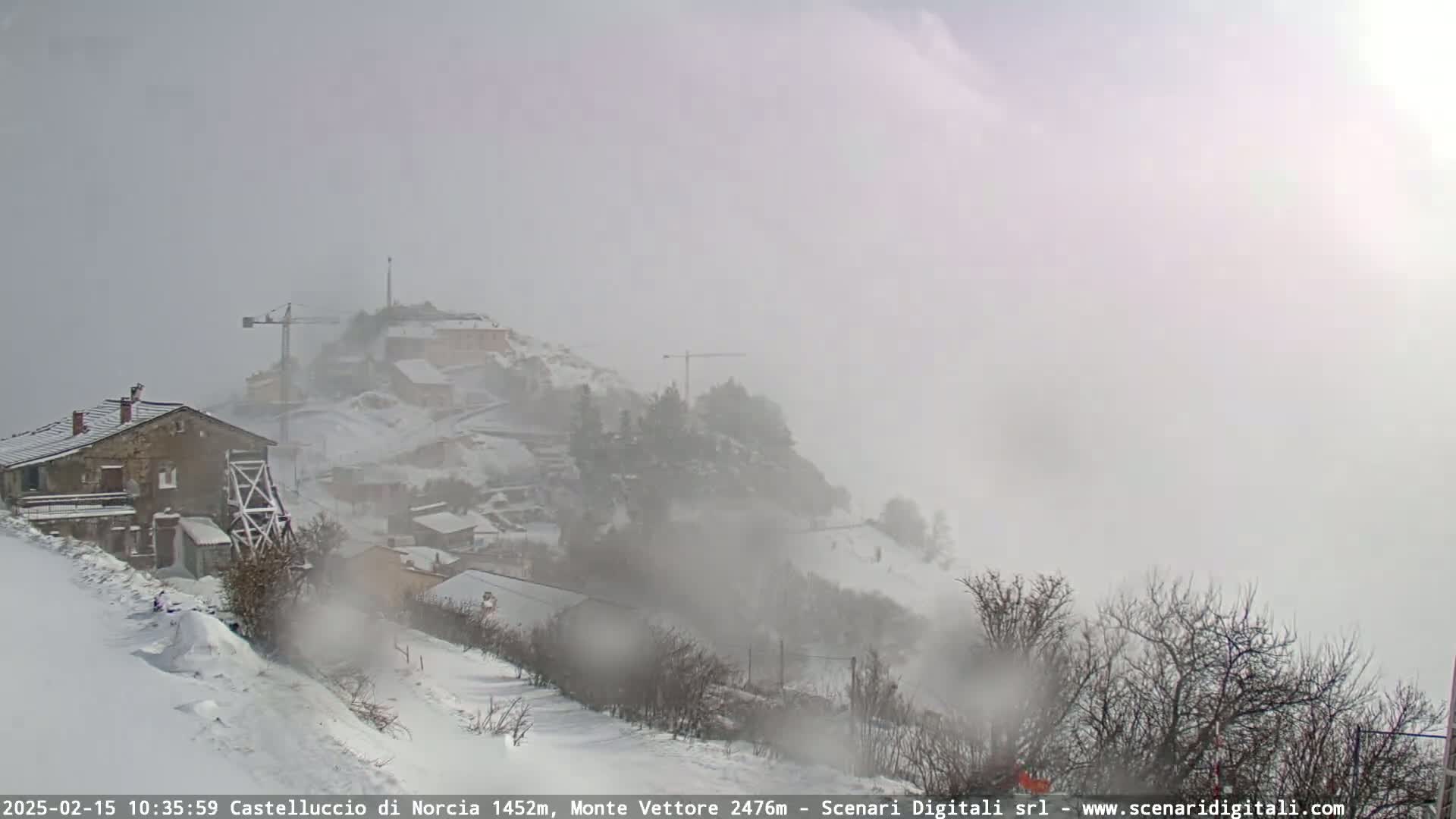 A snow-covered village nestled on a hillside is shrouded in heavy fog and snow.