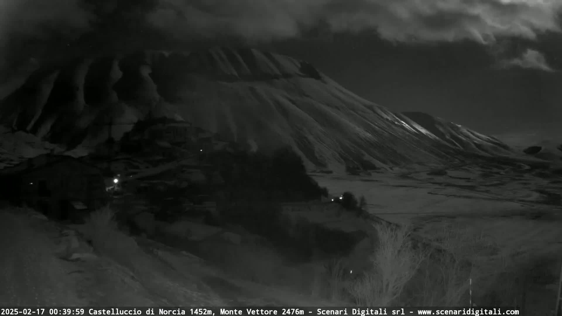 A nighttime view of a snow-covered hillside and small village under a cloudy sky.