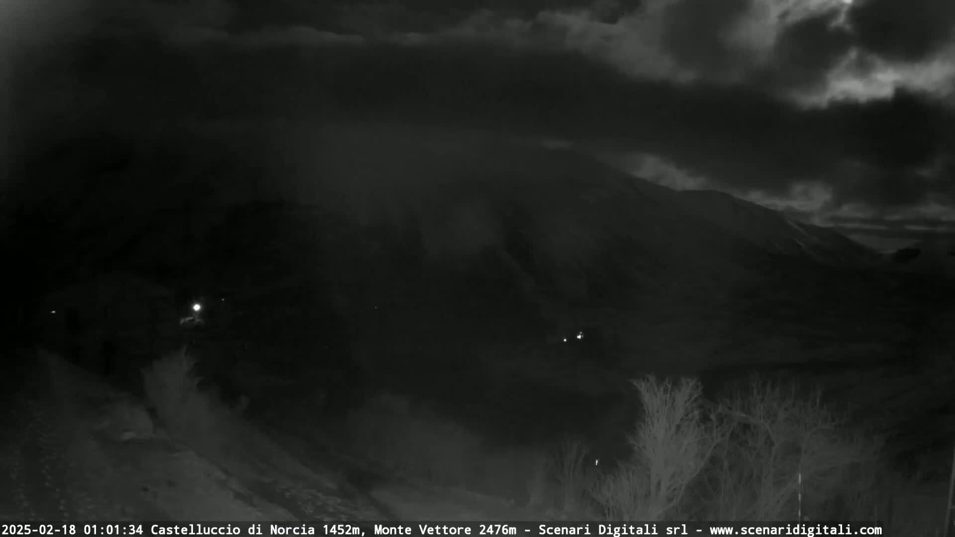 A nighttime, overcast view of a mountain range with sparse vegetation in the foreground.