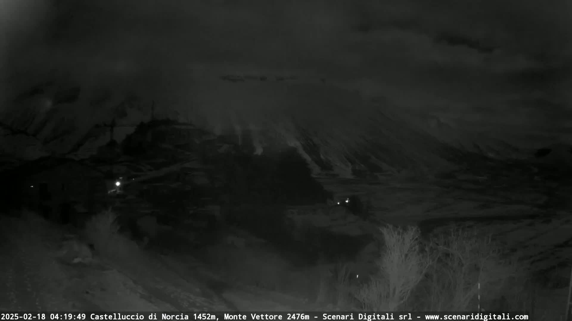 A nighttime, low-light view of a mountainous landscape under a cloudy sky.
