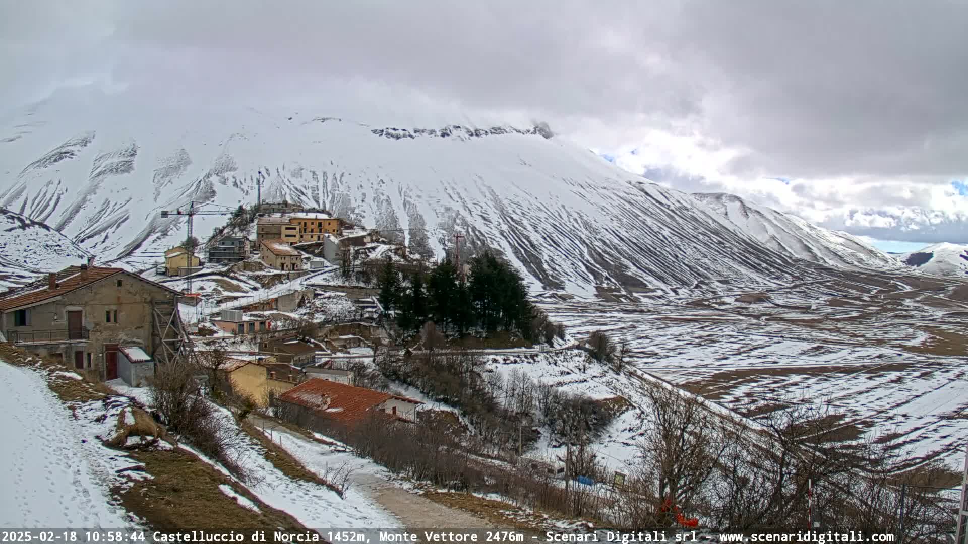 A snow-covered mountain valley with a small village nestled amongst the slopes under a cloudy sky.