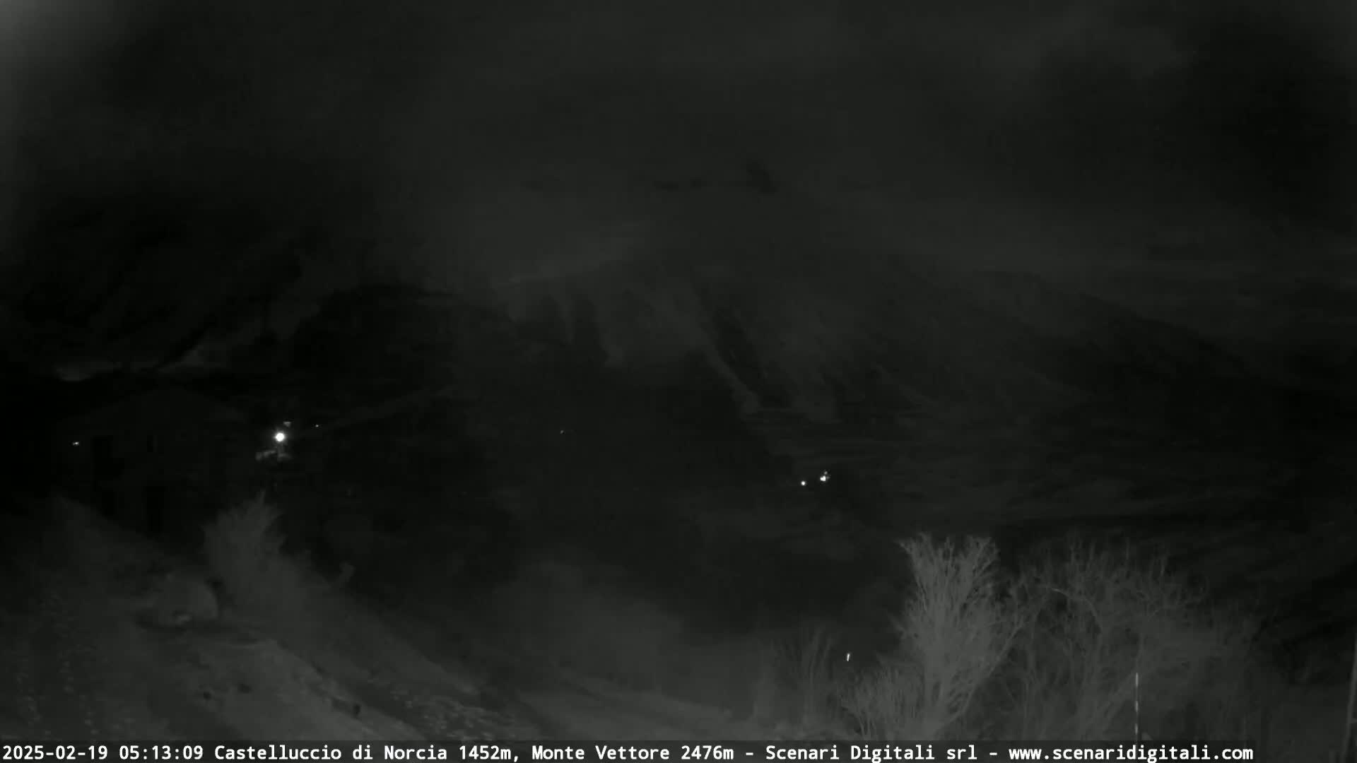 A nighttime, low-light view of a dark, mountainous landscape under a cloudy sky.