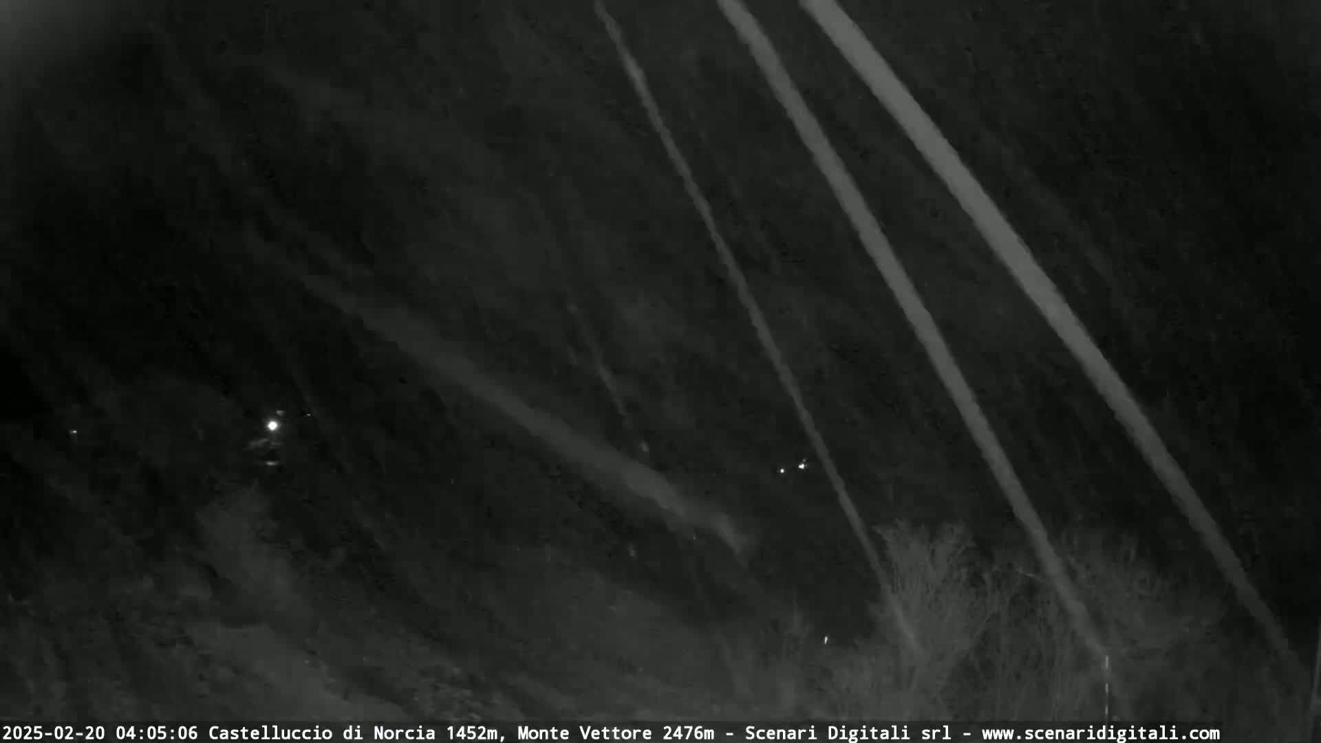 A nighttime, low-light view shows several diagonal streaks of light against a dark, mountainous landscape.