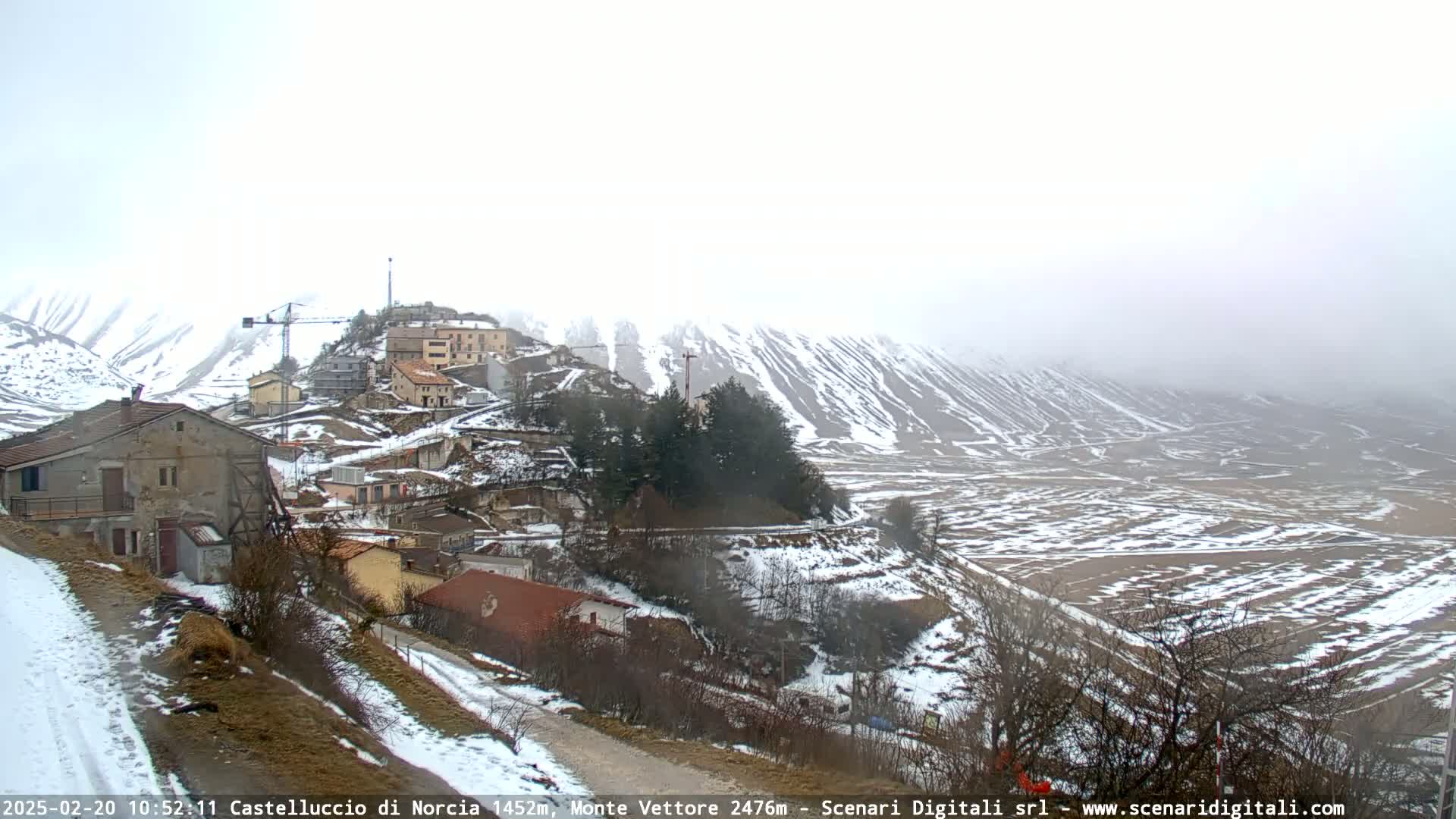 A snow-covered village nestled in a mountainous valley under a foggy sky.