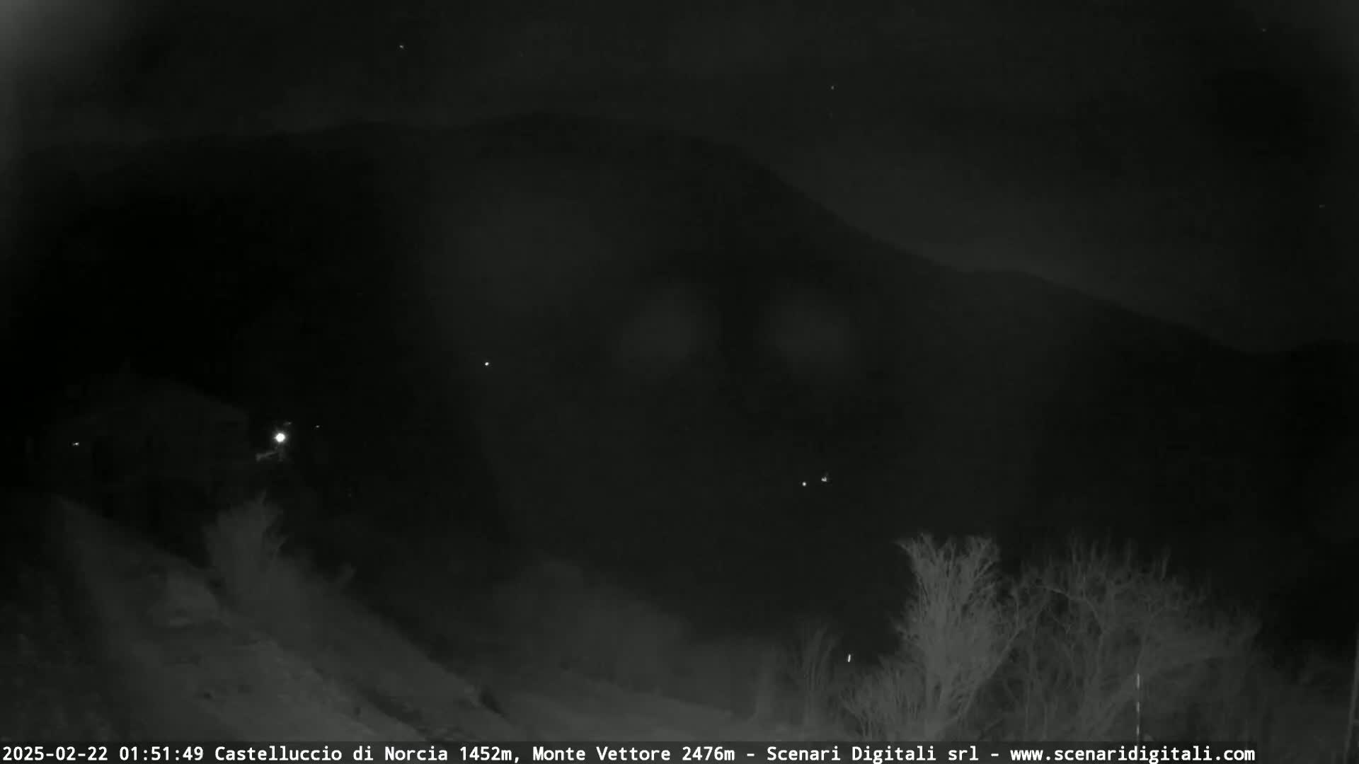 A nighttime, low-light image shows a dark mountain silhouetted against a dark sky dotted with a few visible stars.