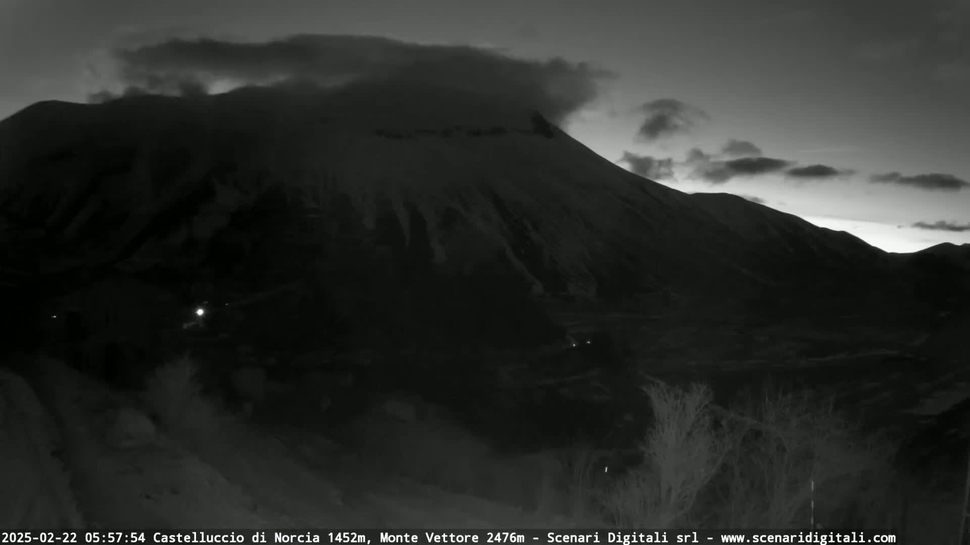 A dark, snow-dusted mountain is partially obscured by clouds under a twilight sky.