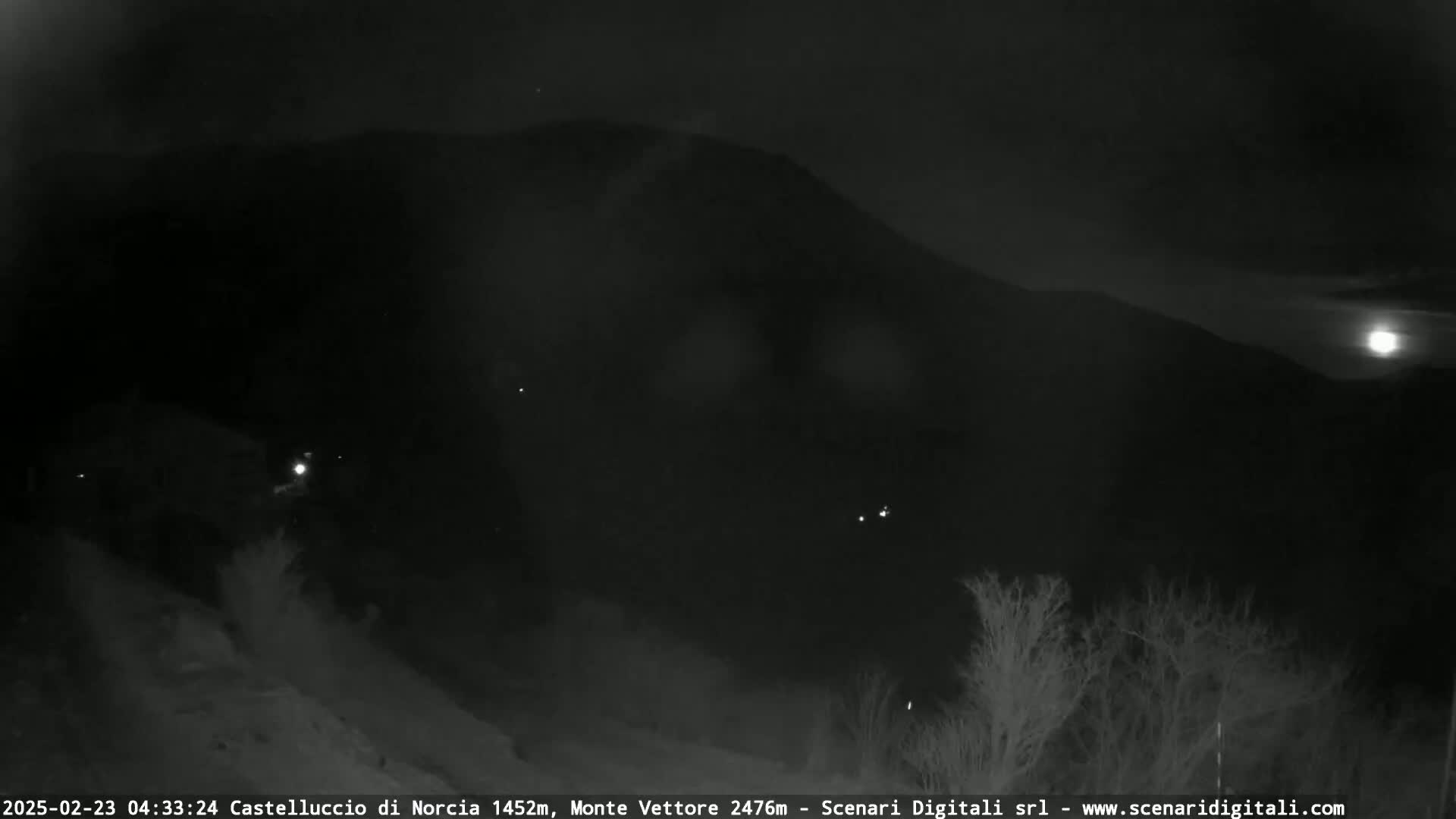 A nighttime view of a dark mountain range under a partially visible moon.