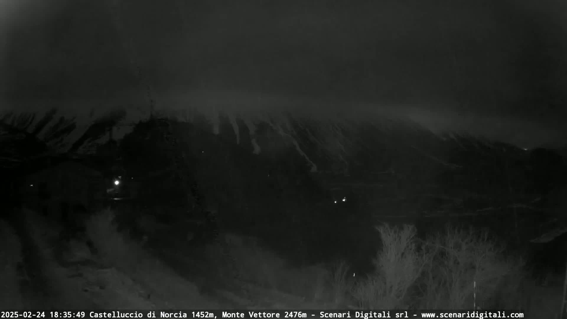 A nighttime, low-visibility view of a snow-covered mountain shrouded in fog or mist.