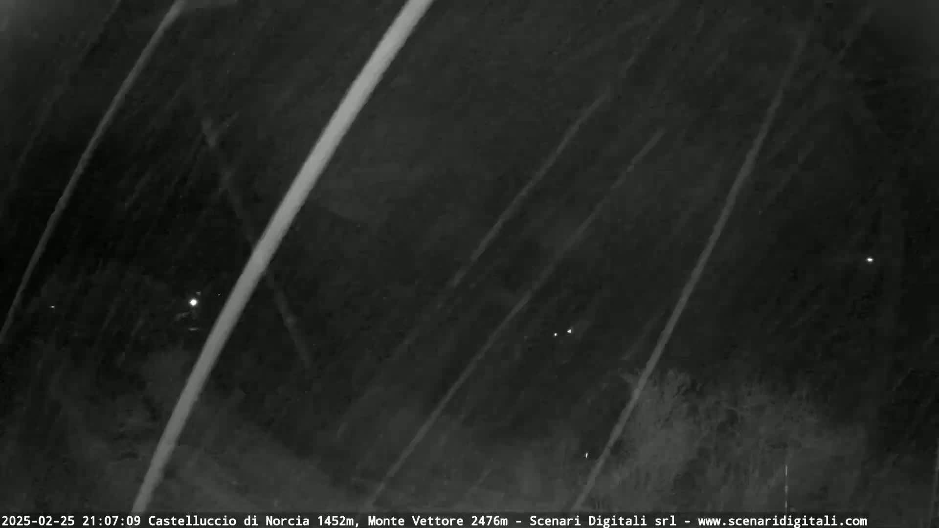 A nighttime, snowy scene shows faint lights in the distance and streaks of snow falling diagonally across the frame.