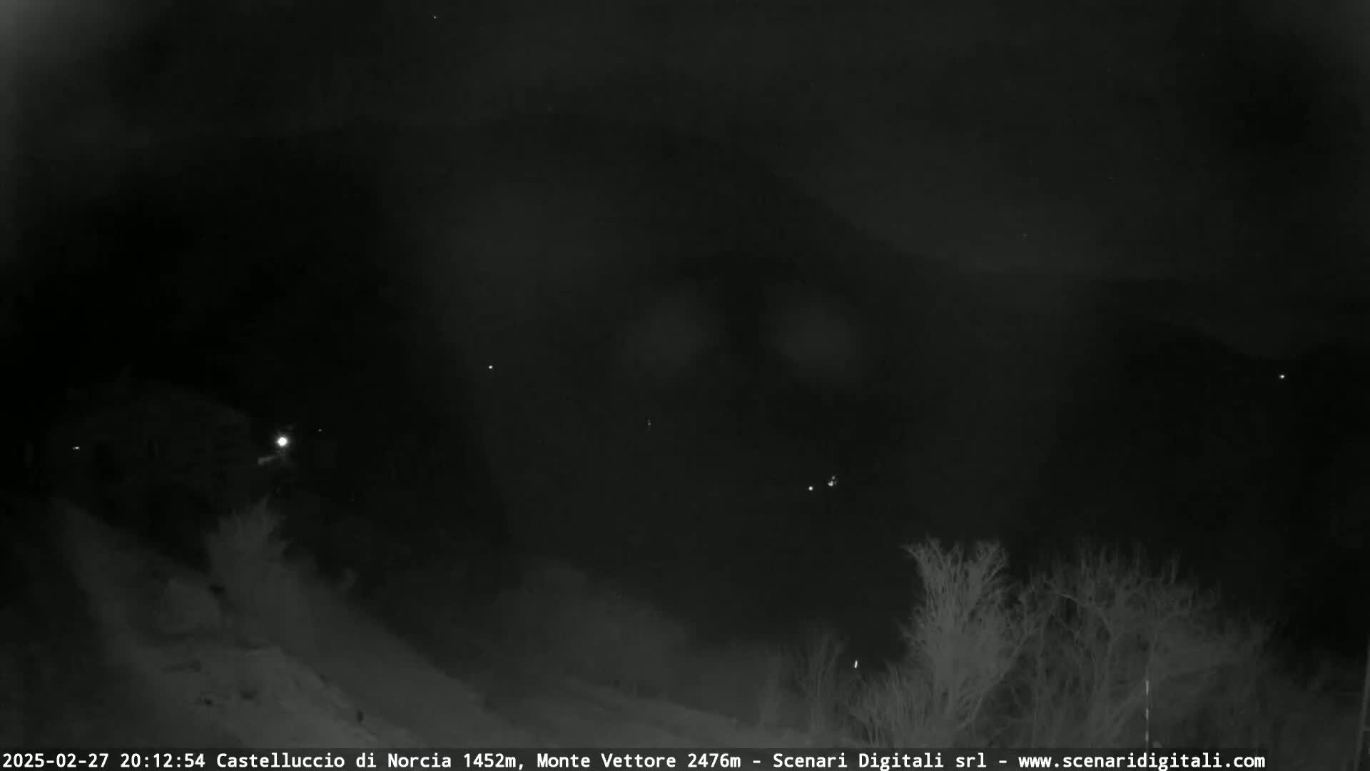 A nighttime, snowy landscape is visible under a dark, cloudy sky with a few distant lights.