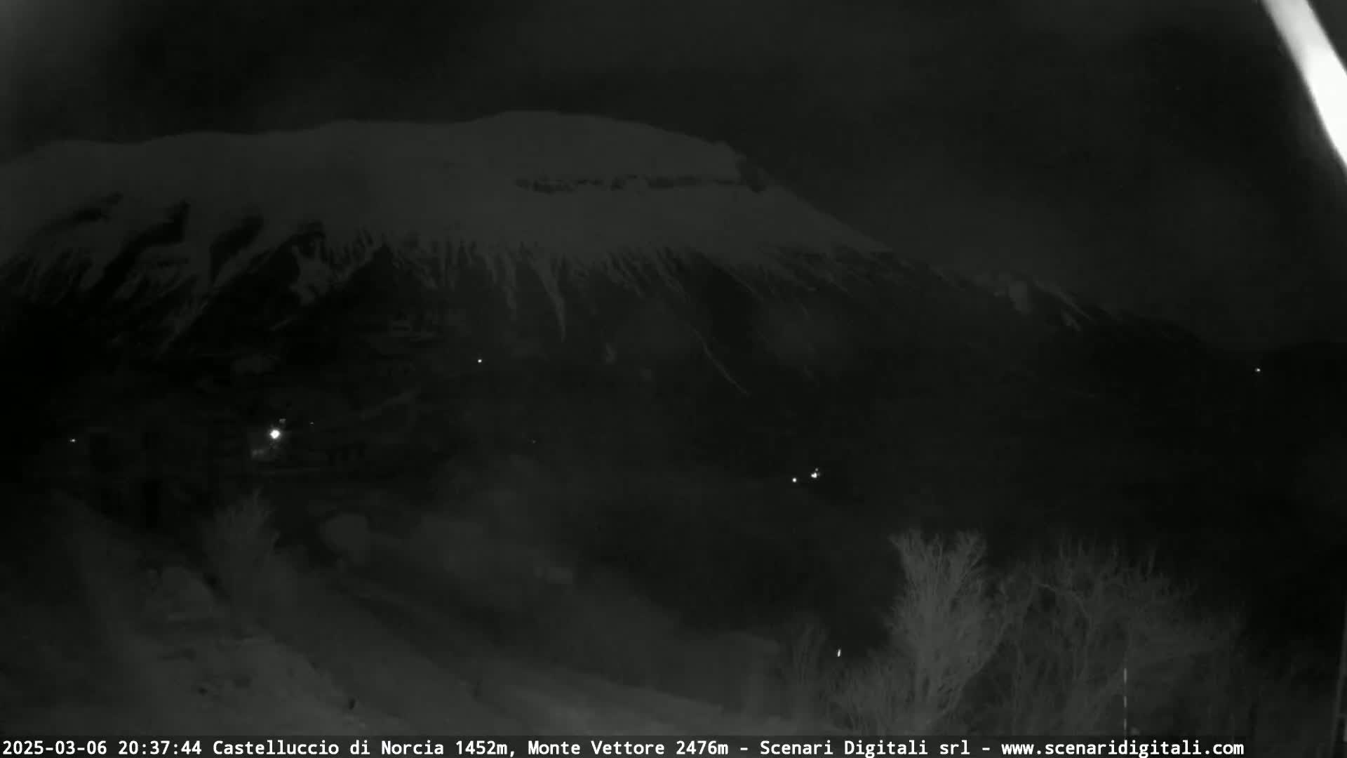 A nighttime view of a snow-covered mountain range under a dark sky.