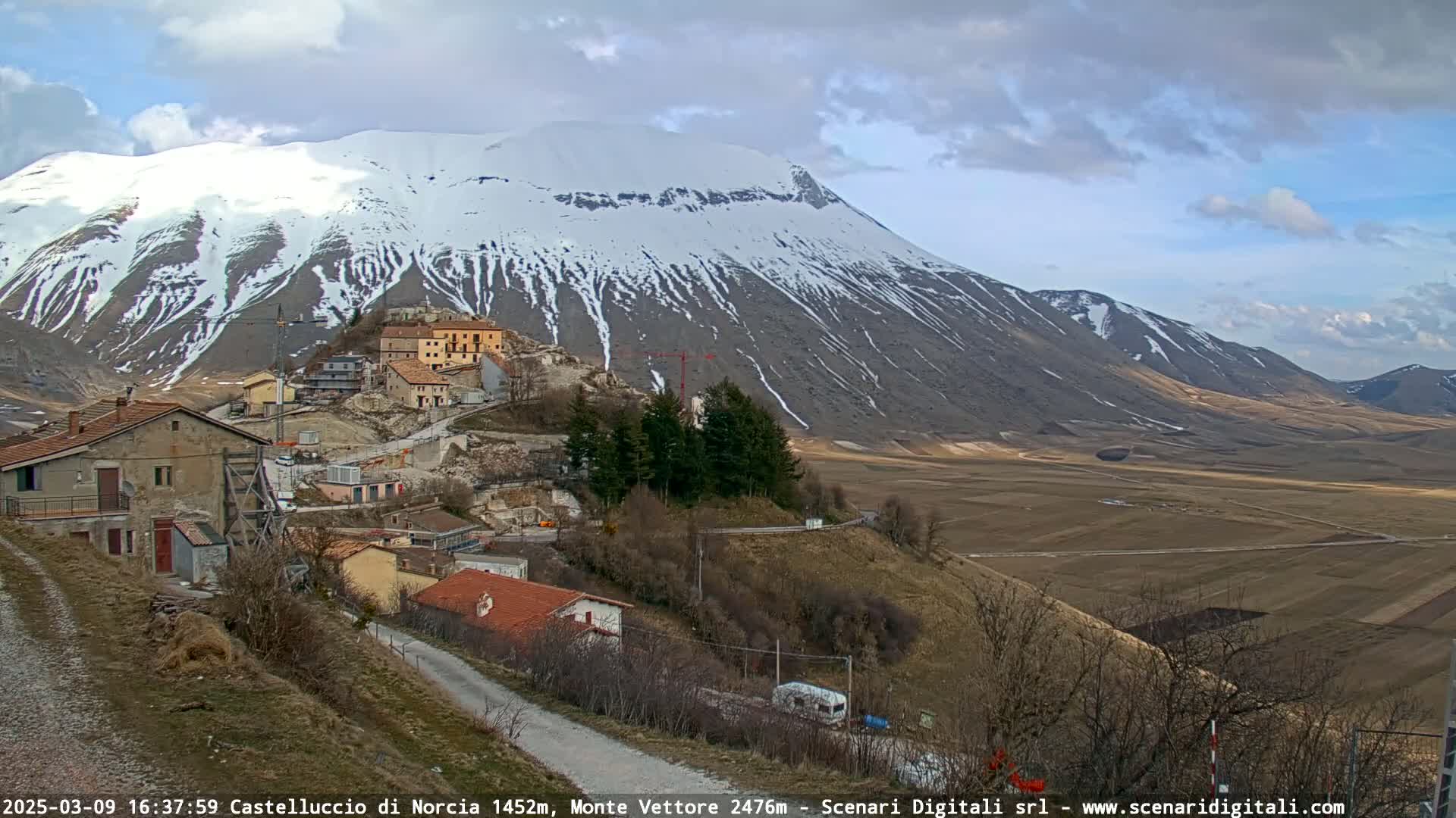 A small village nestled at the base of a snow-capped mountain under a partly cloudy sky.