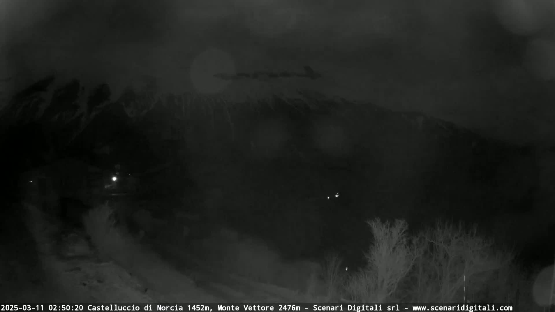 A nighttime, low-visibility view of a snow-covered mountain range under a dark sky.