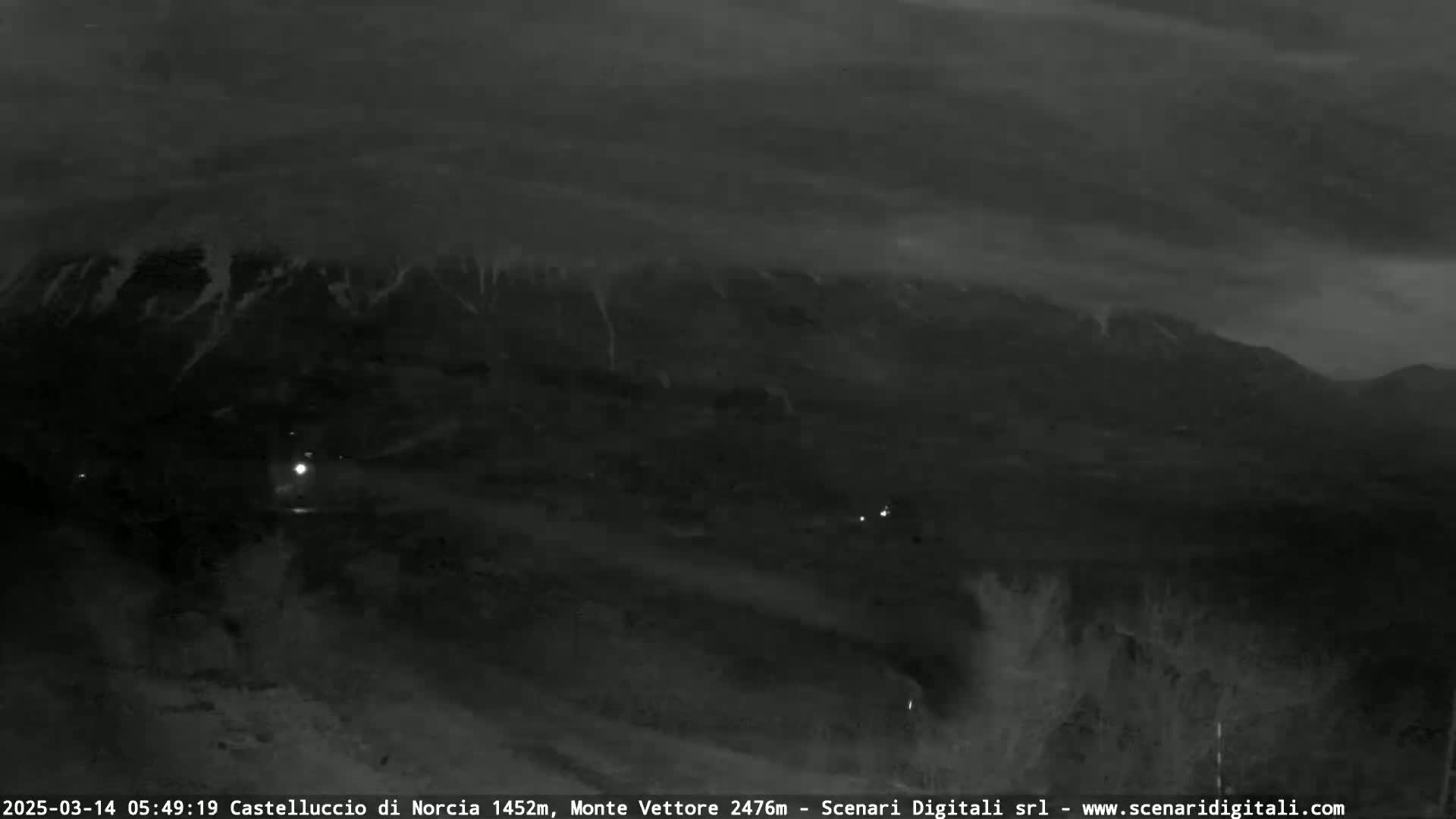 A nighttime, low-light image shows a dark mountain range under a cloudy sky.
