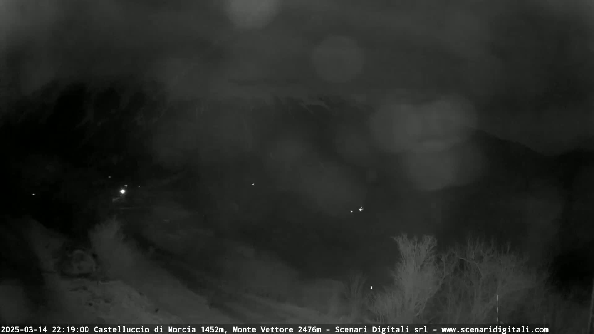 A nighttime, blurry view of a snow-covered landscape with a few distant lights visible through a hazy atmosphere.
