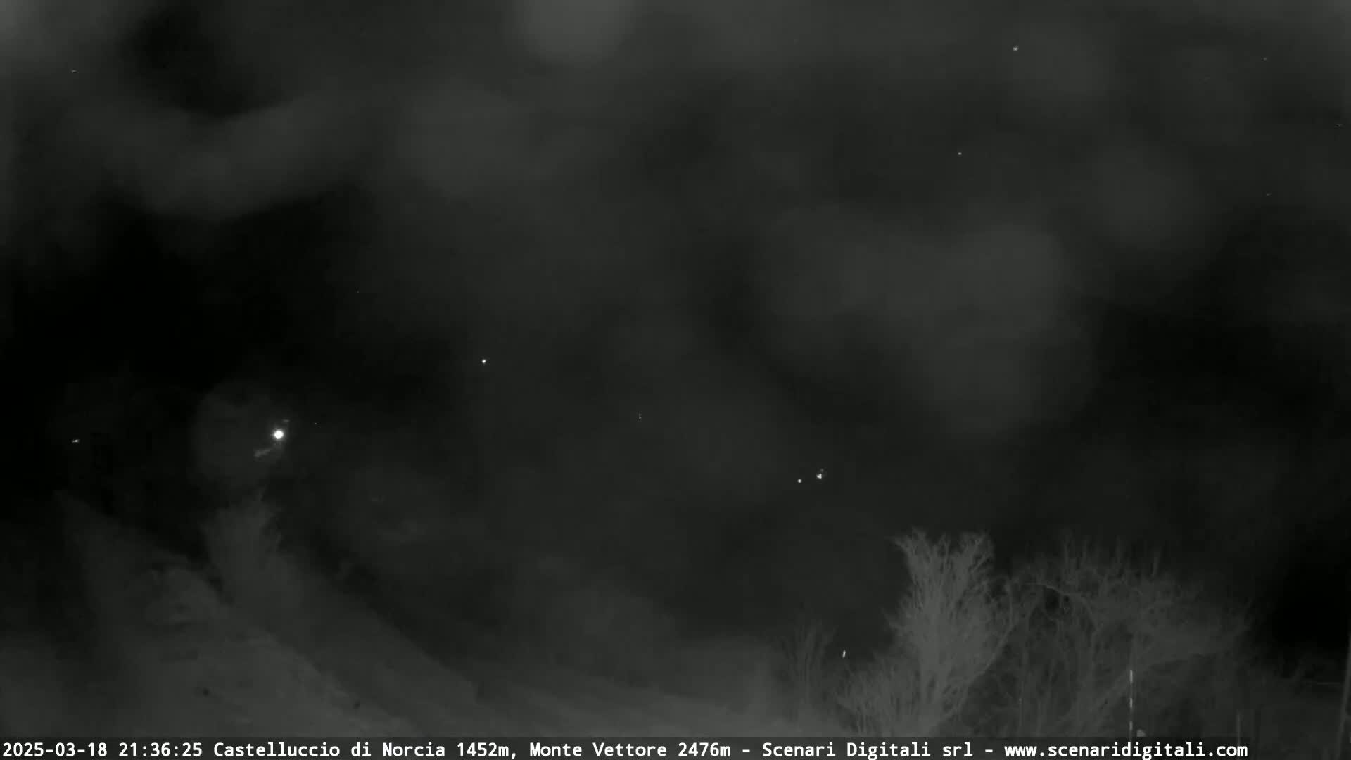 A nighttime, low-light view shows a dark, cloudy sky above a sparsely vegetated landscape.