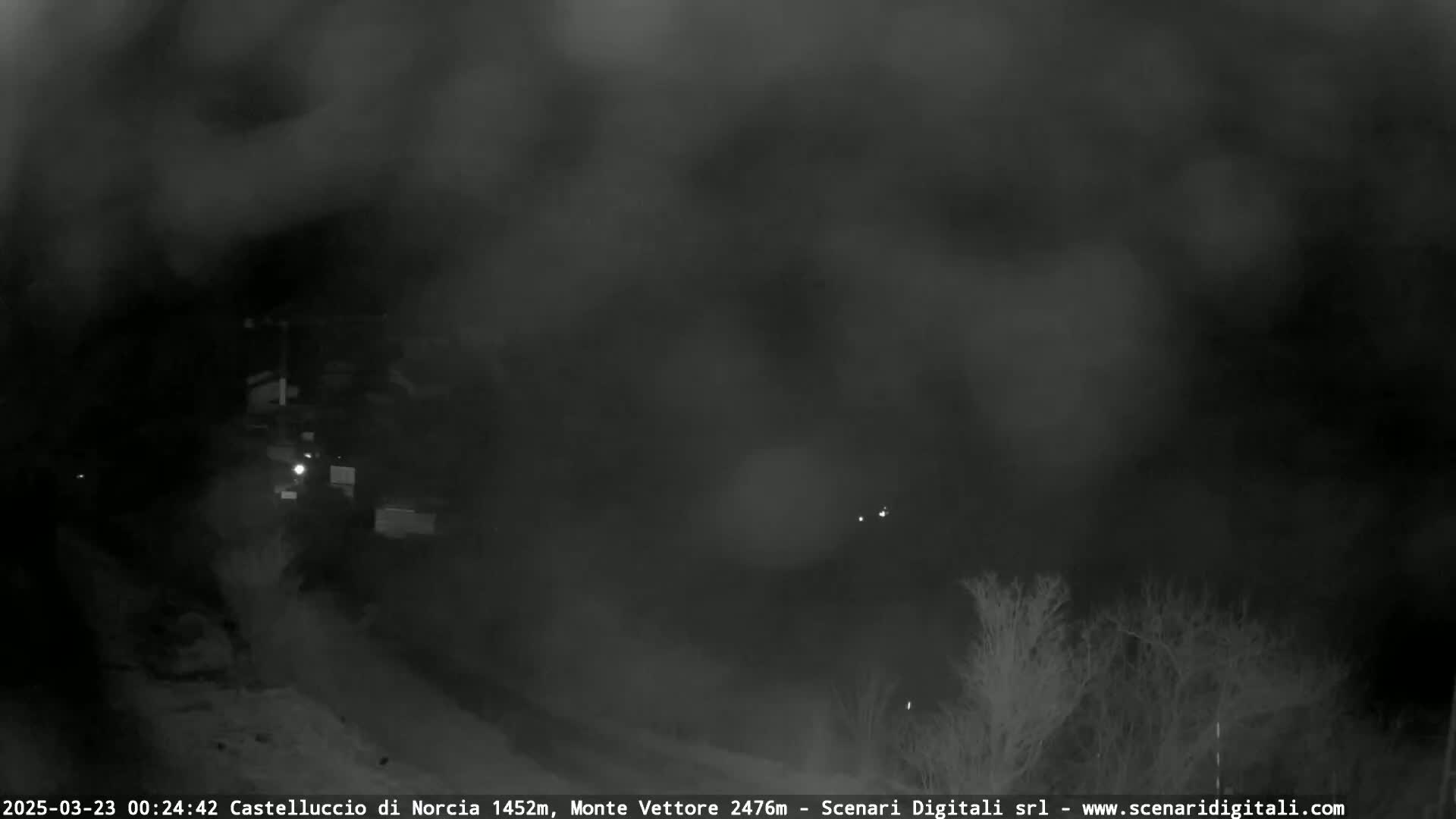 A nighttime, blurry view of a sparsely lit landscape shrouded in heavy fog or mist.