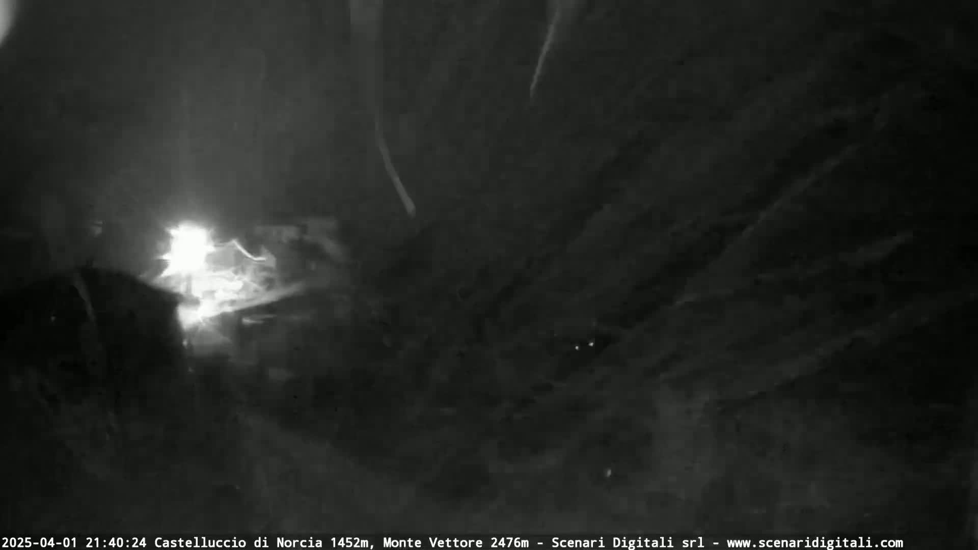 A nighttime, low-light image shows a bright light source in the center, possibly lightning, amidst a dark, possibly stormy sky.