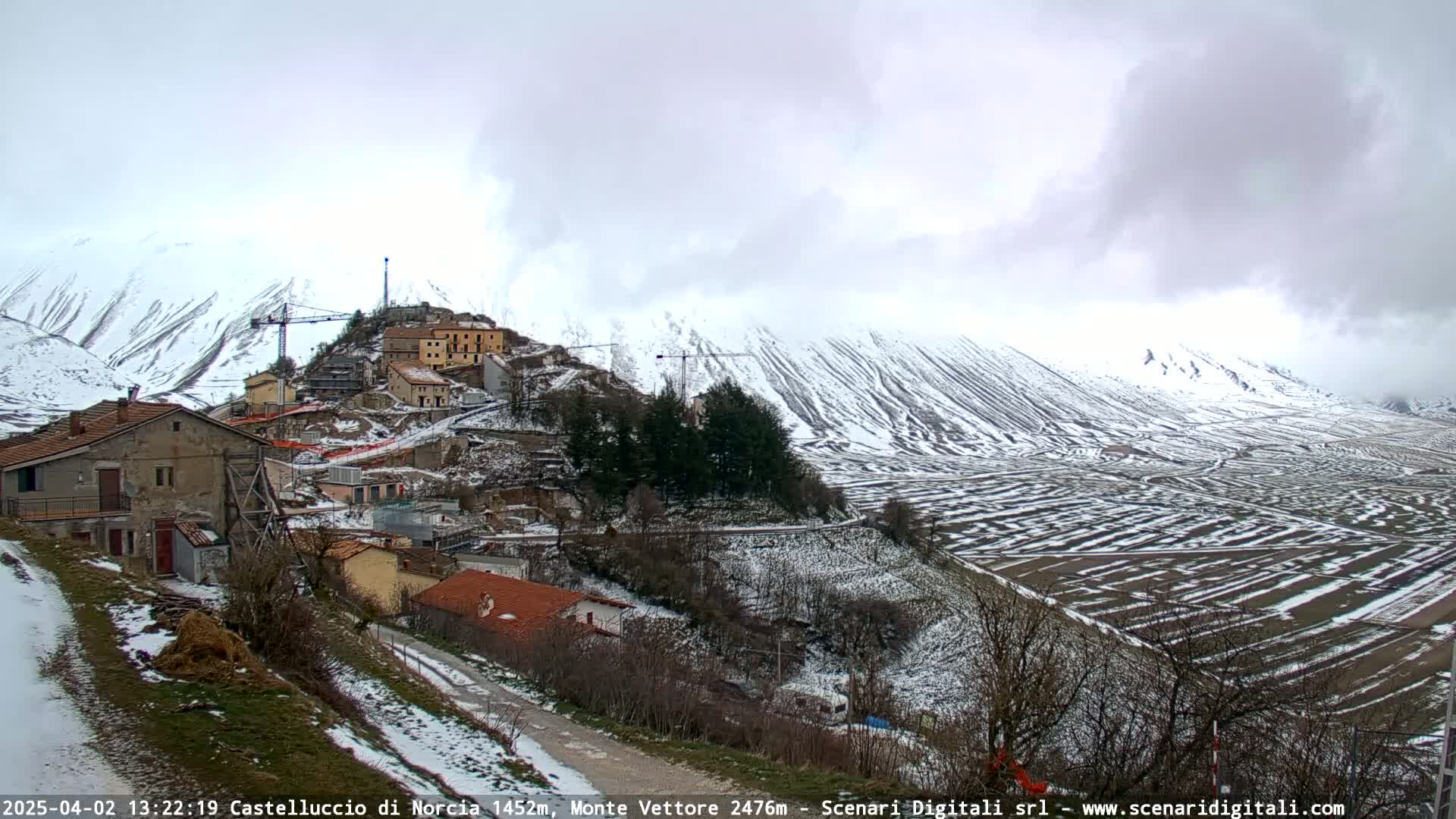 A snow-covered village nestled in a valley between snow-dusted mountains under a cloudy sky.