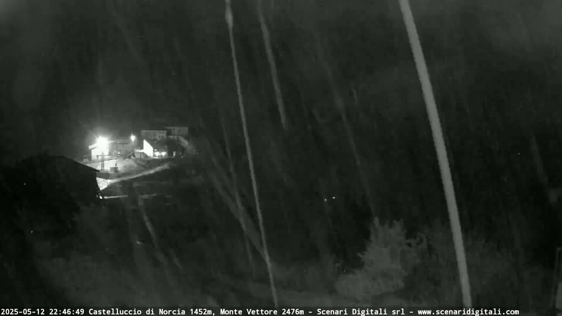 A nighttime, blurry view of a small settlement under heavy rain or snow.