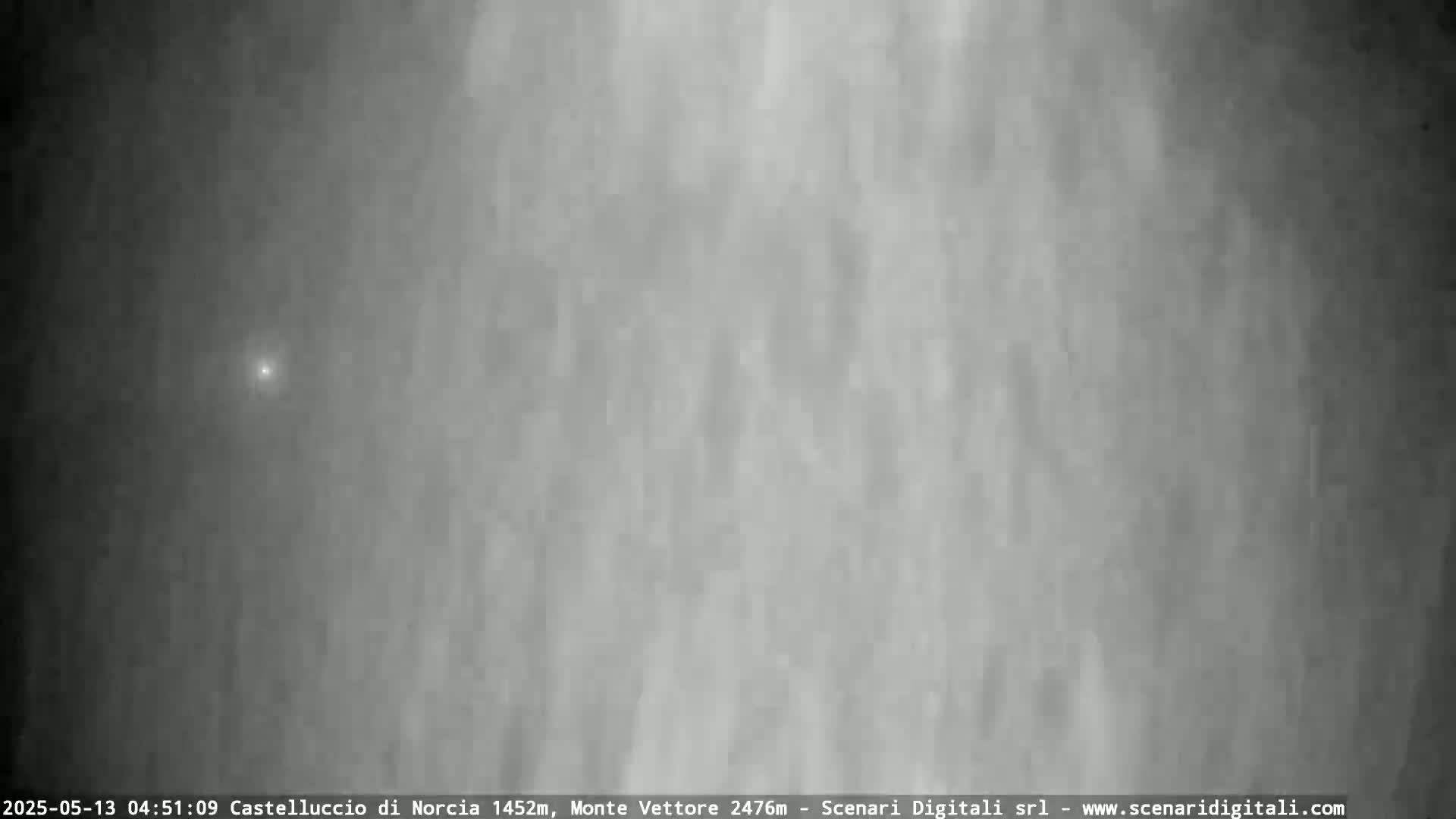 A single, small, bright light is visible in a gray, cloudy sky.